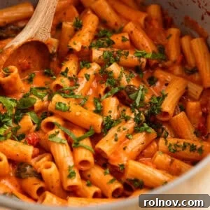 Creamy one pot tomato pasta in pot with wooden spoon.