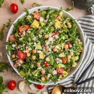 Chickpea avocado salad in bowl with arugula, feta, cucumbers, tomato and other ingredients.