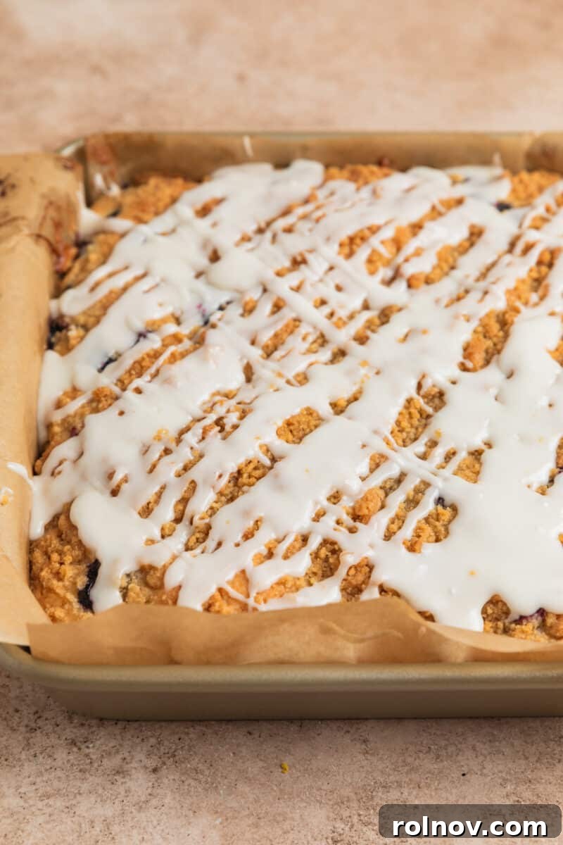 Bright and Zesty Blueberry Lemon Coffee Cake 17 Icing drizzled over top of coffee cake in parchment lined pan.