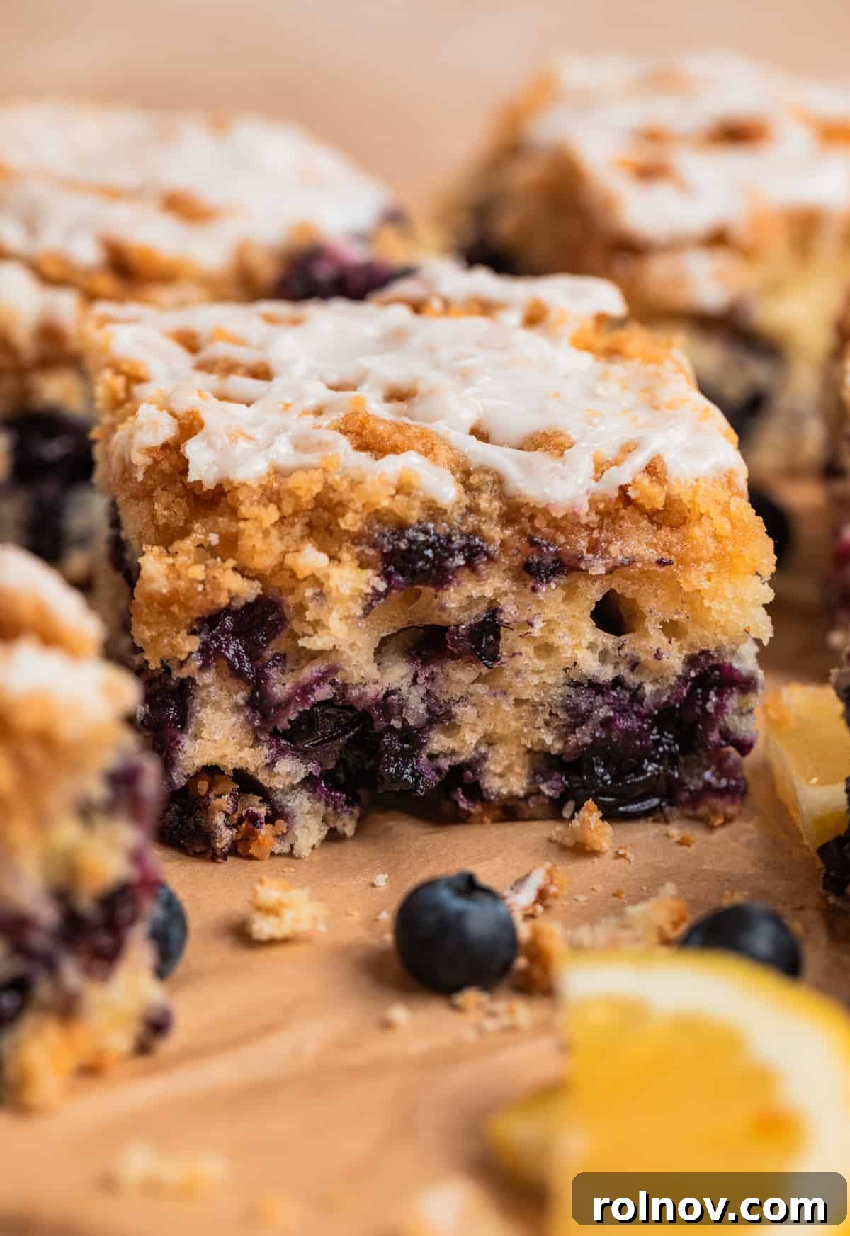 Bright and Zesty Blueberry Lemon Coffee Cake 4 Slice of blueberry coffee cake with icing over top and lemons and fresh blueberries beside it.