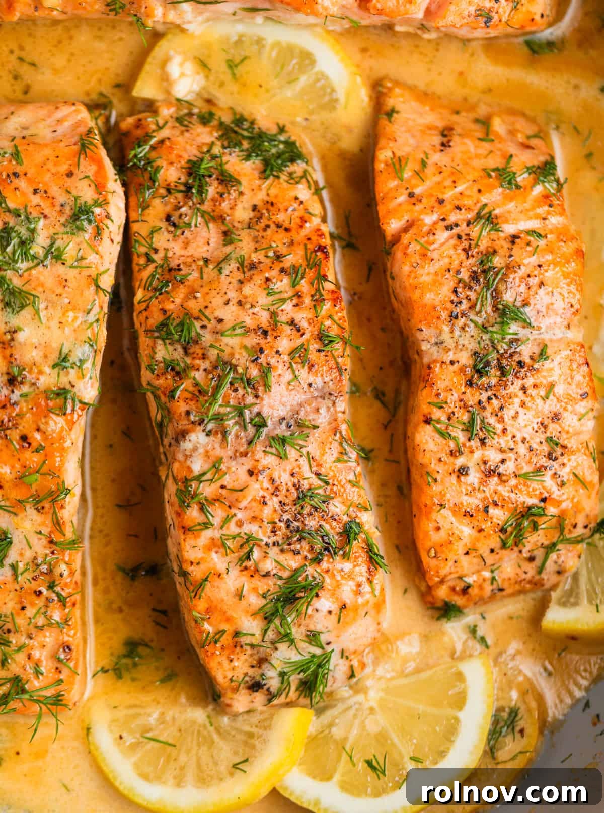 Zesty Lemon Dill Salmon 2 Overhead view of pan seared salmon fillets topped with fresh dill and lemon slices in pan.