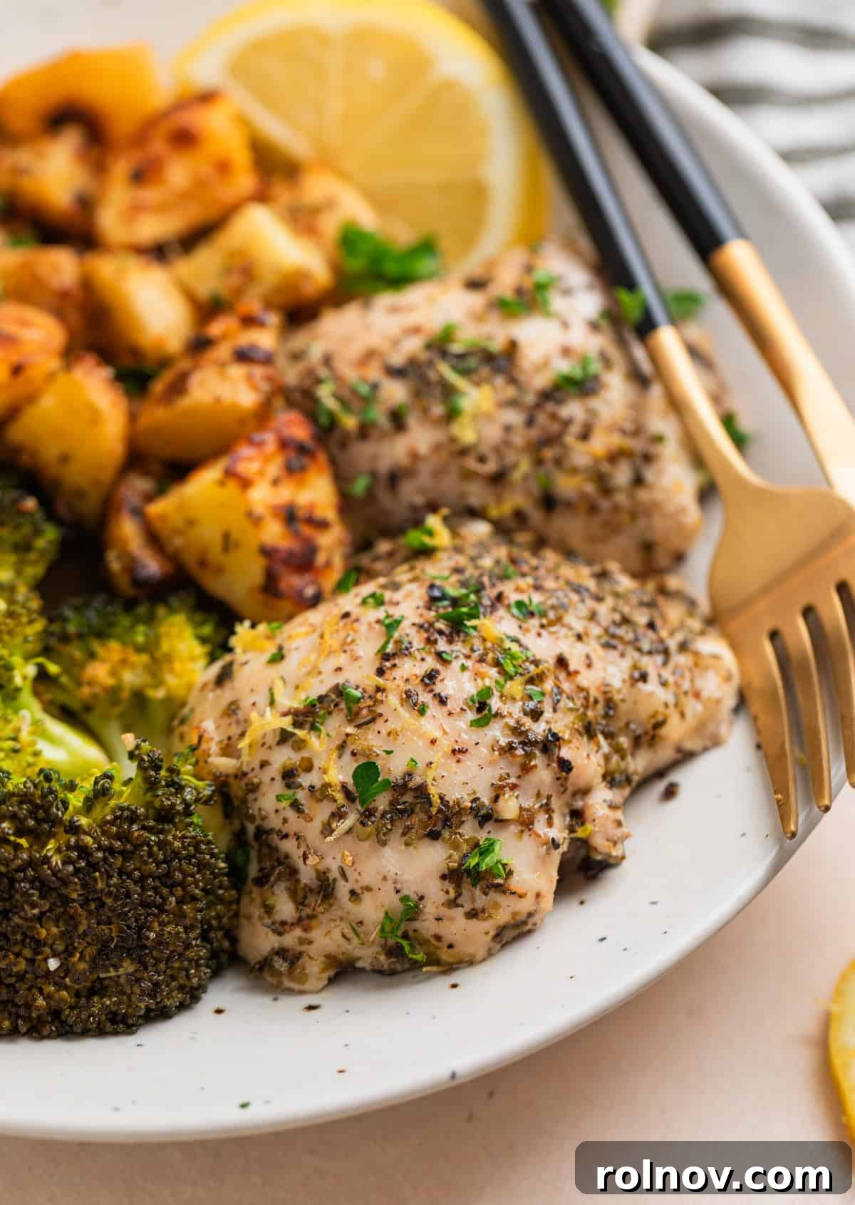 Lemon herb chicken thighs on white plate with crispy potatoes wedges and broccoli.