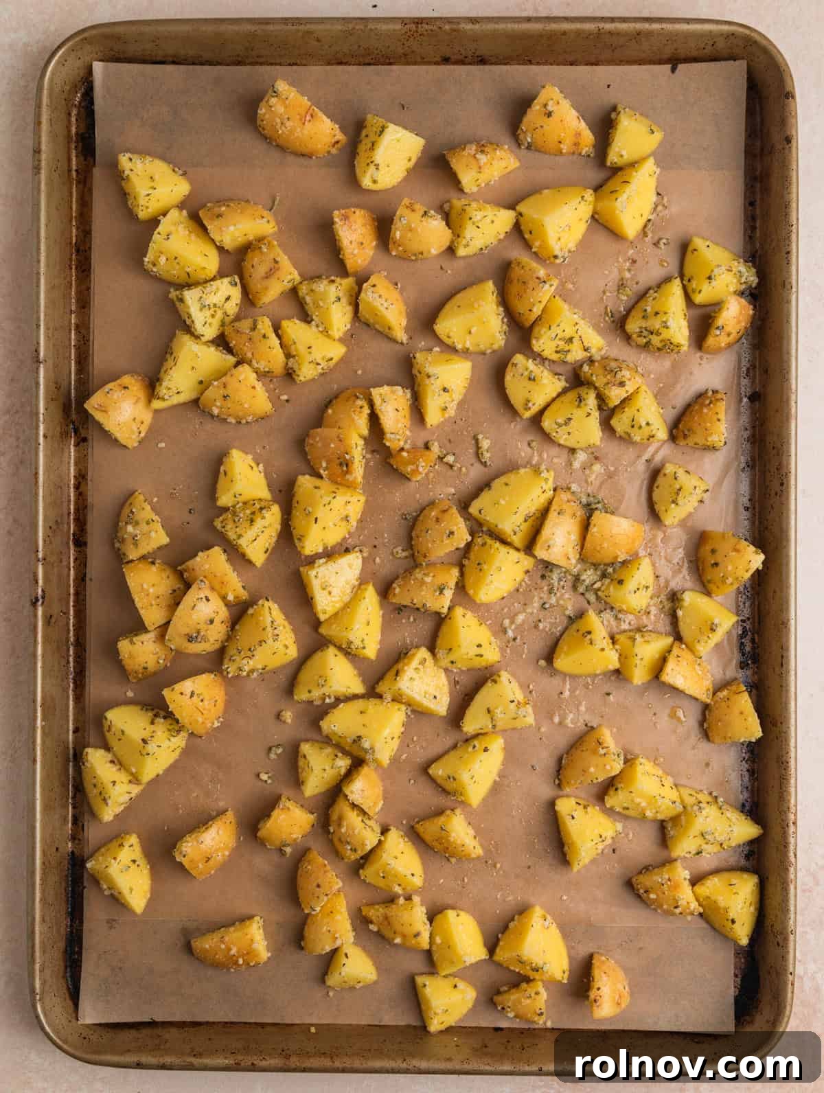 Parmesan, oil and herbed potato pieces lined on sheet pan.