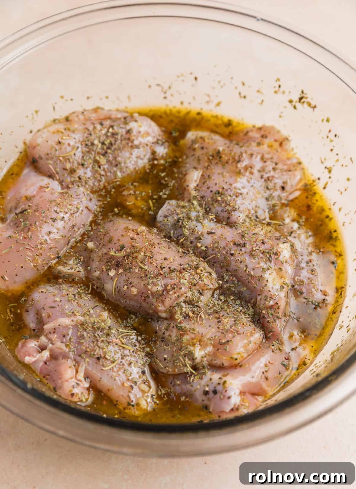 Boneless skinless chicken thighs in lemon marinade in glass bowl.