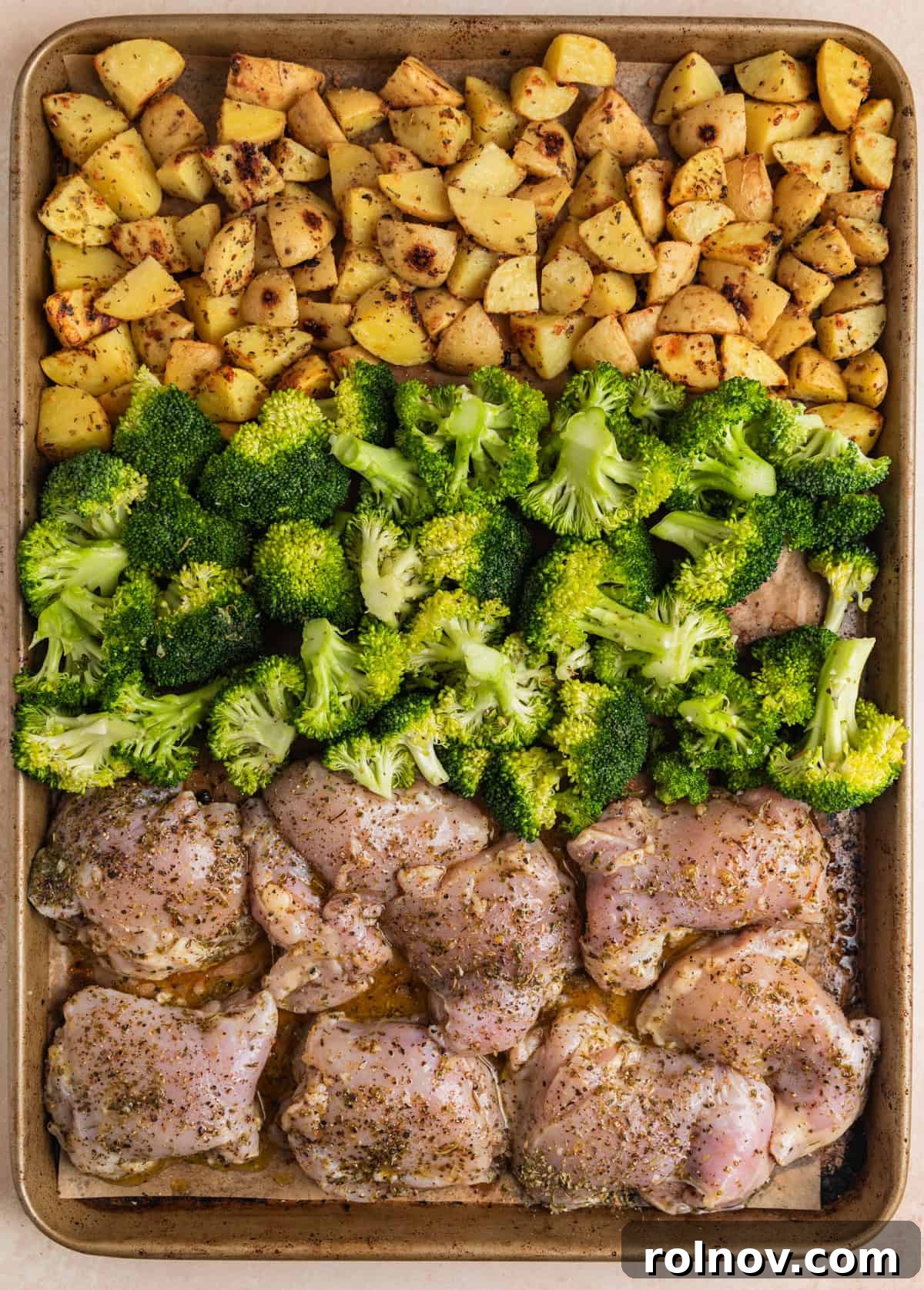 Uncooked chicken thighs and broccoli added to sheet pan with potatoes already partially roasted.