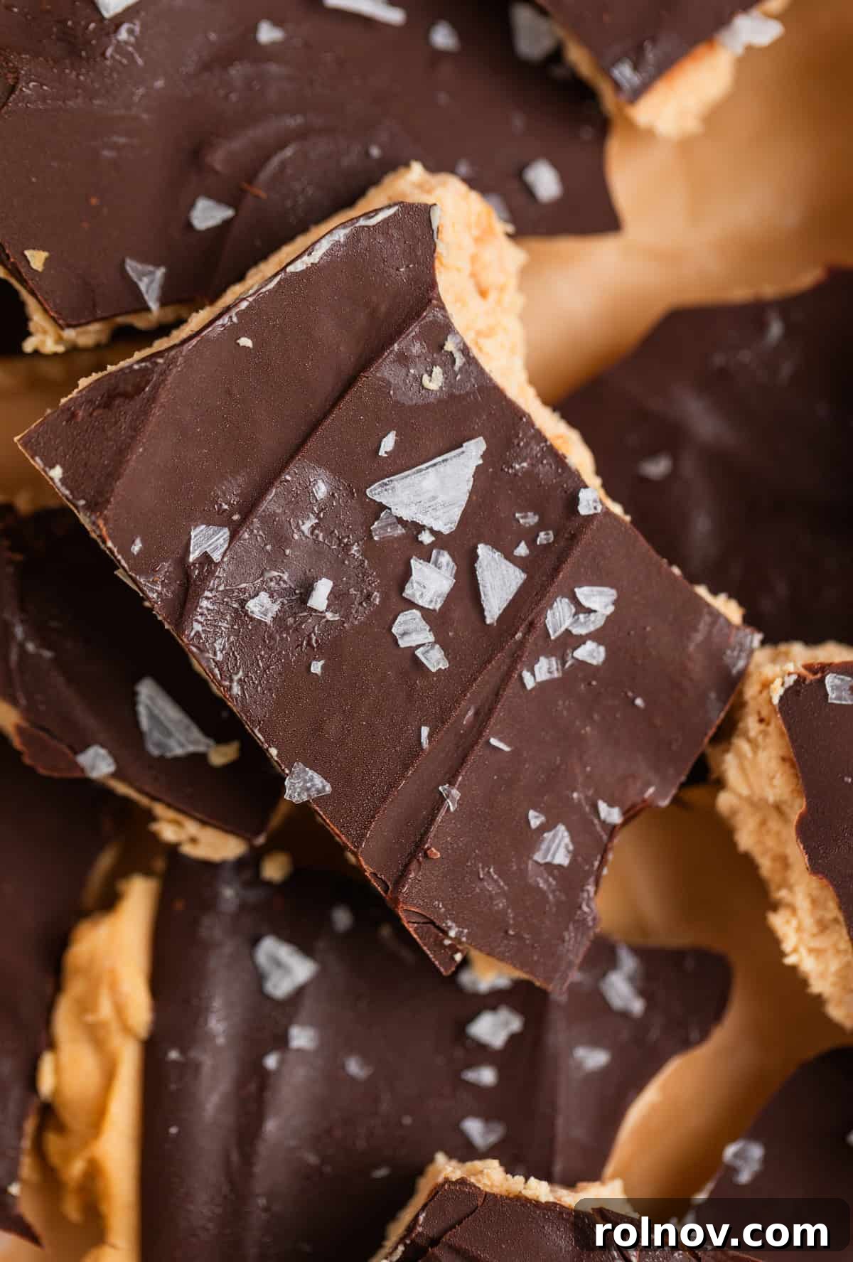 Frozen Greek Yogurt Bites 9 Close up of frozen chocolate covered peanut butter yogurt bark scattered on parchment paper, highlighting its delicious texture and salt flakes.
