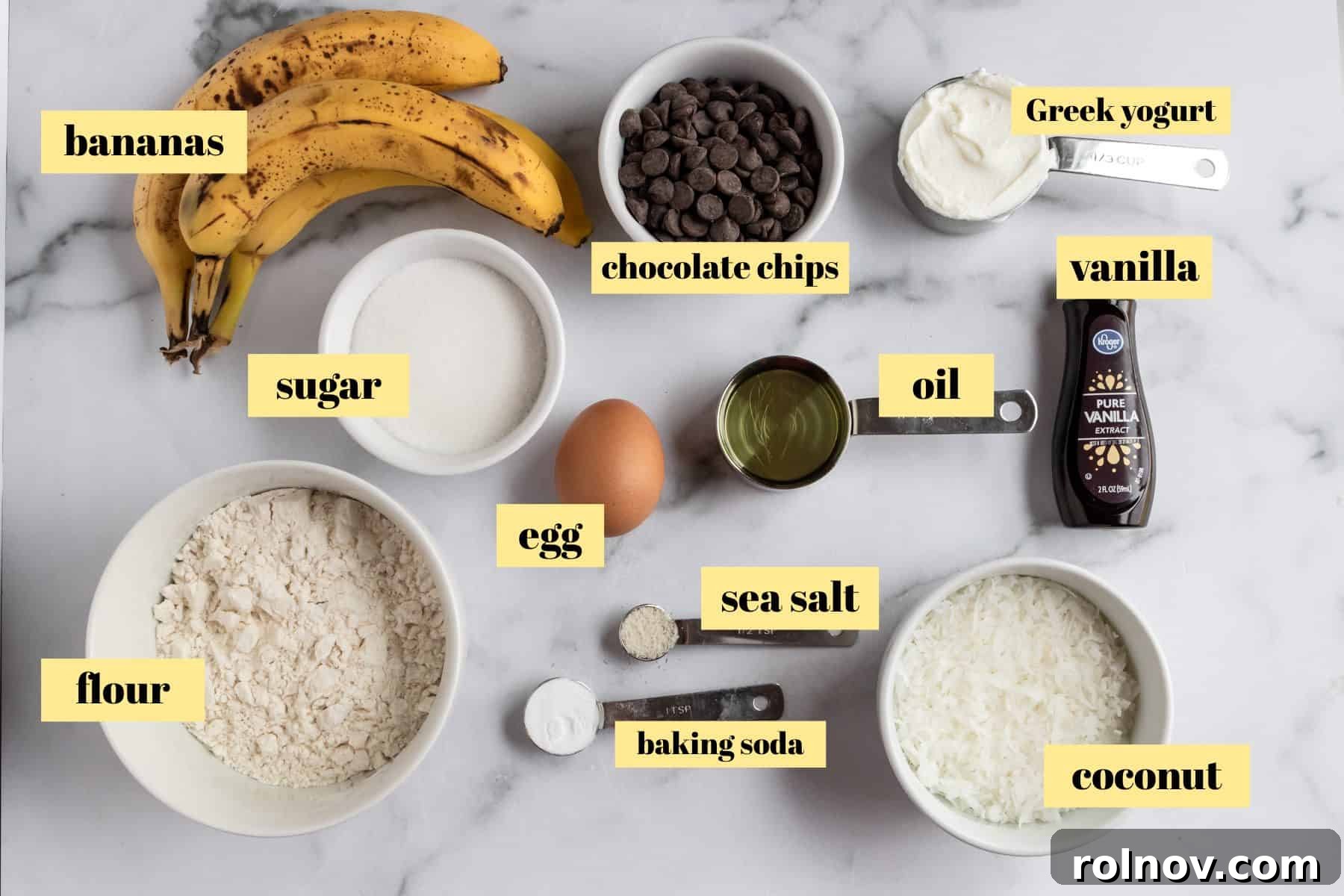 Tropical Banana Chocolate Chip Muffins 4 Various ingredients laid out on a countertop, including bananas, flour, sugar, oil, yogurt, vanilla, salt, baking soda, coconut, and chocolate chips, ready for baking muffins.