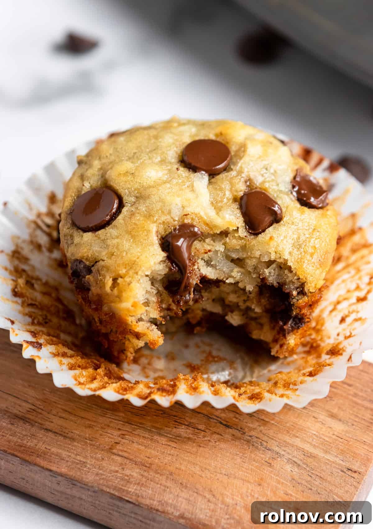 Tropical Banana Chocolate Chip Muffins 10 A freshly baked coconut banana muffin with its paper liner partially removed, revealing its moist texture.