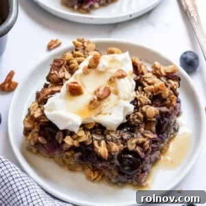 Slice of blueberry baked oatmeal on white plate with maple syrup.
