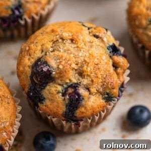 Blueberry muffin with coarse sugar on top and crumbs and berries surrounding.