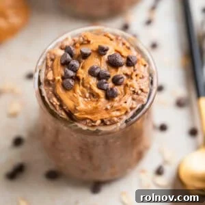 Chocolate chip and peanut butter topped chocolate overnight oats in glass with spoon beside it.