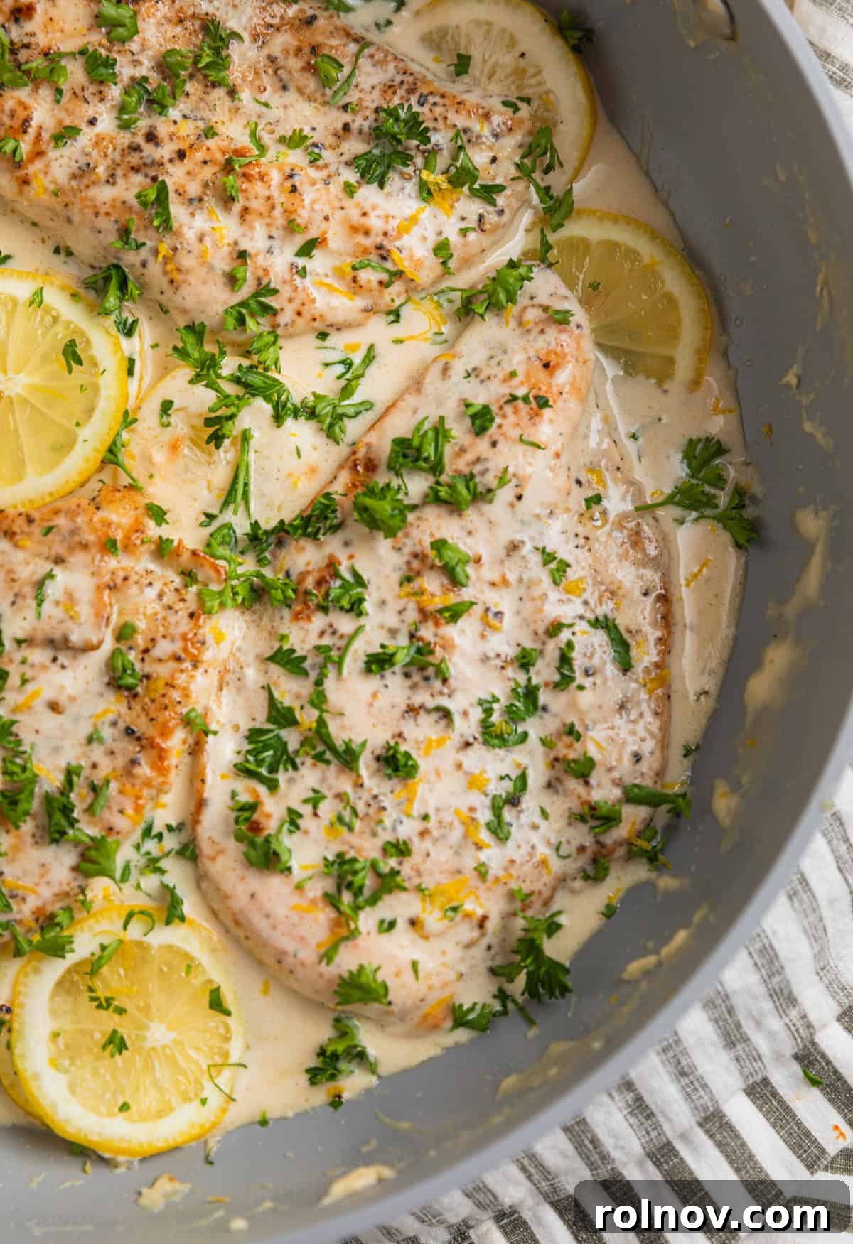 Skillet with creamy lemon chicken topped with chopped parsley.