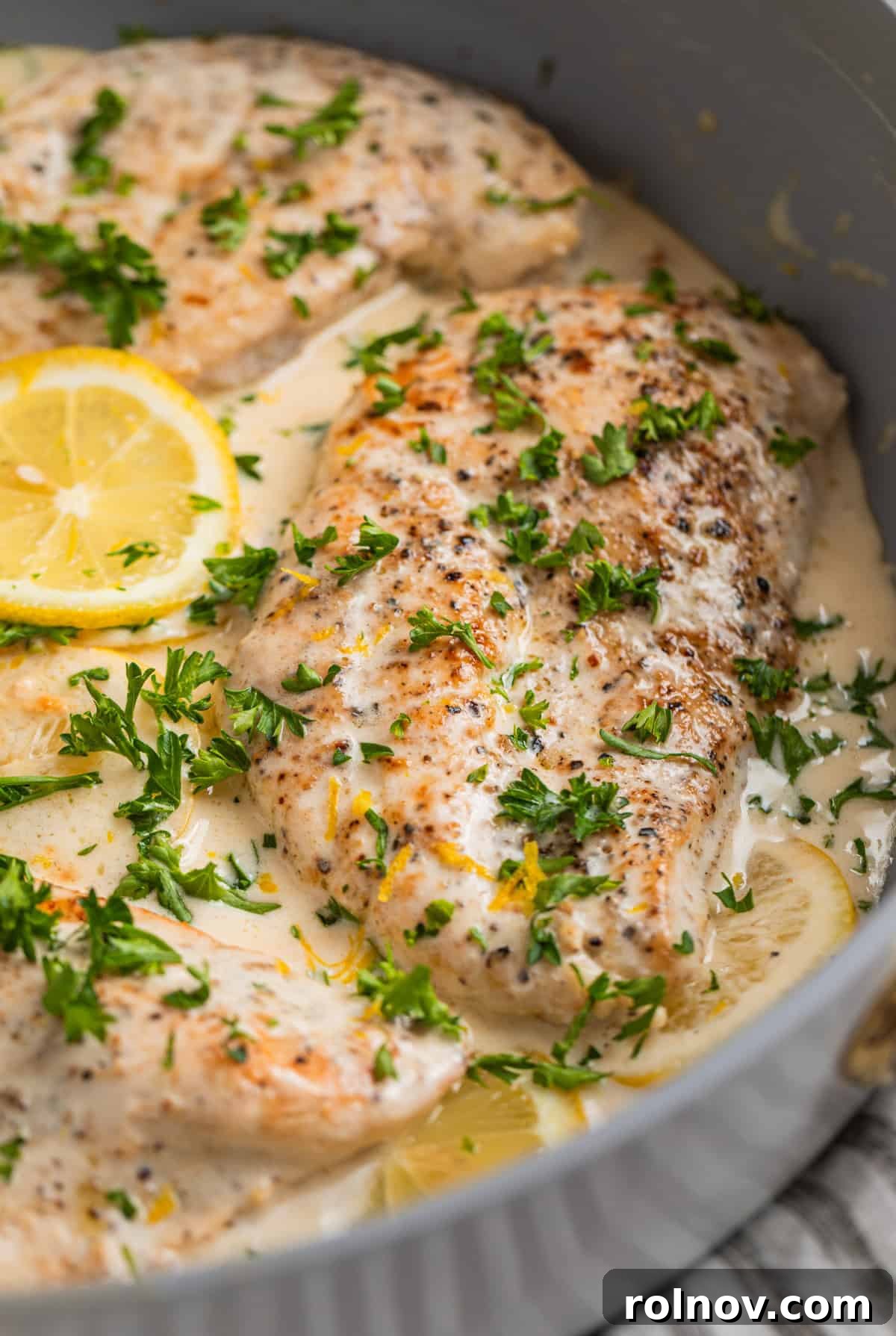 Pan with chicken topped with cream sauce with lemon slices and fresh parsley.