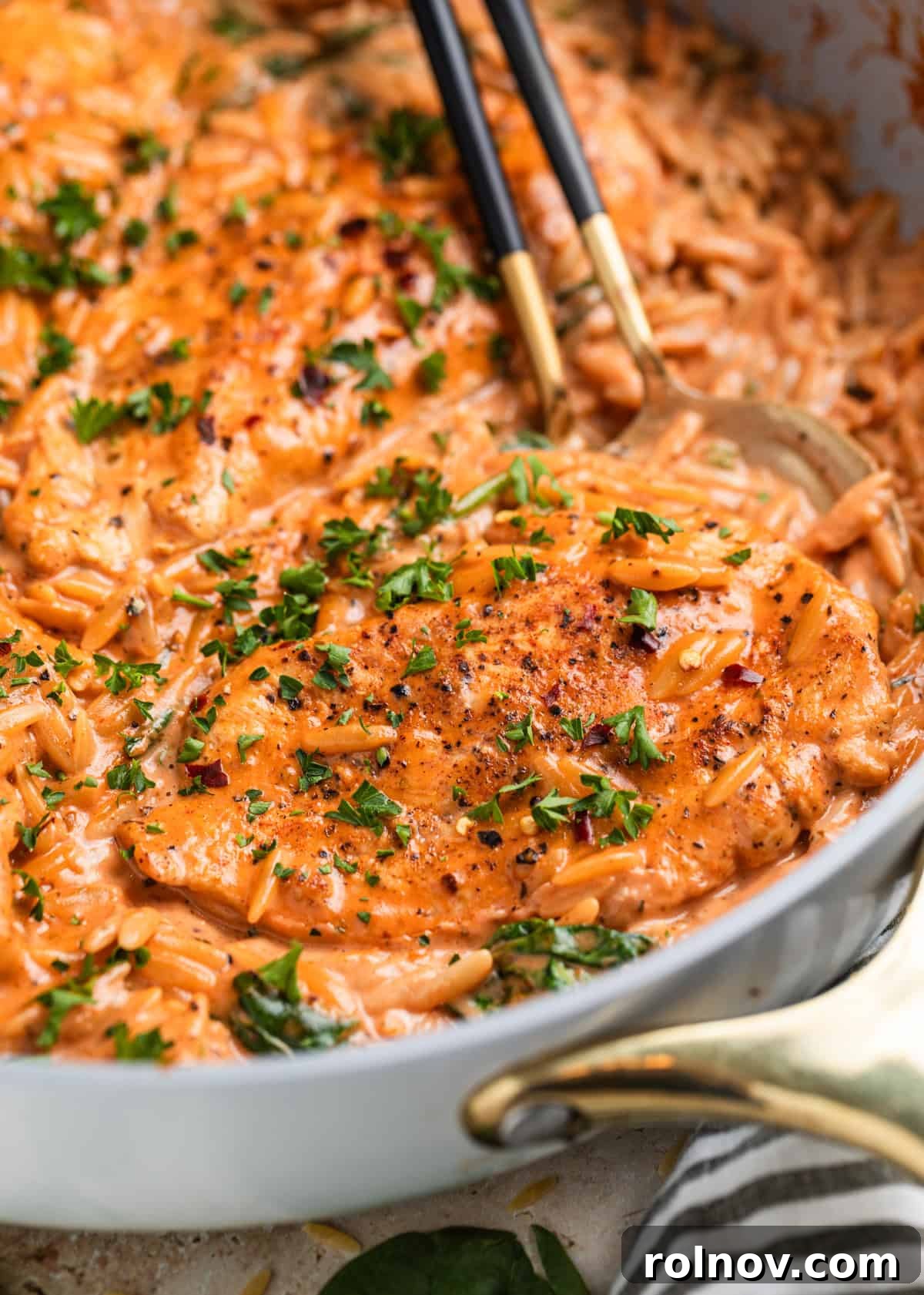Rich Creamy Chicken Orzo 2 Chicken breast in a creamy tomato orzo in skillet with spoons and topped with chopped parsley.