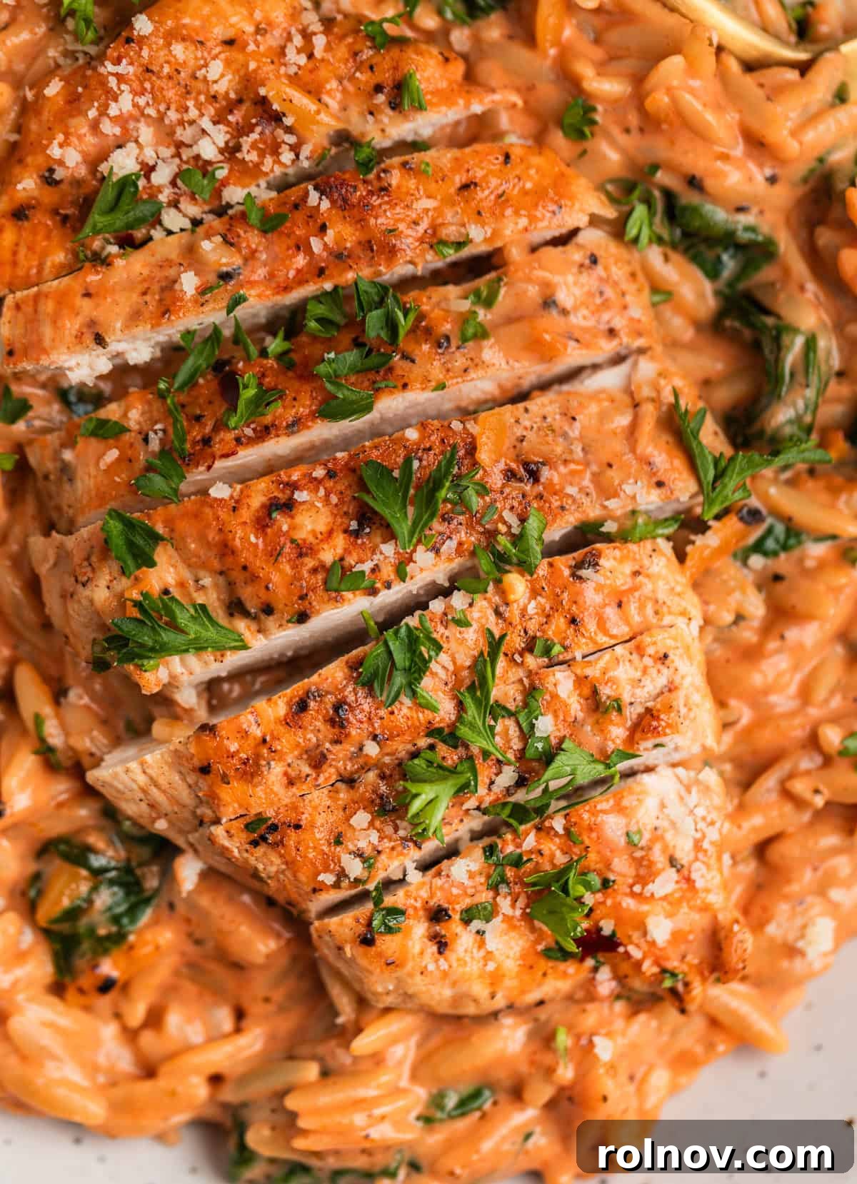 Rich Creamy Chicken Orzo 12 Sliced chicken breast laying on a bed of pasta with chopped parsley.