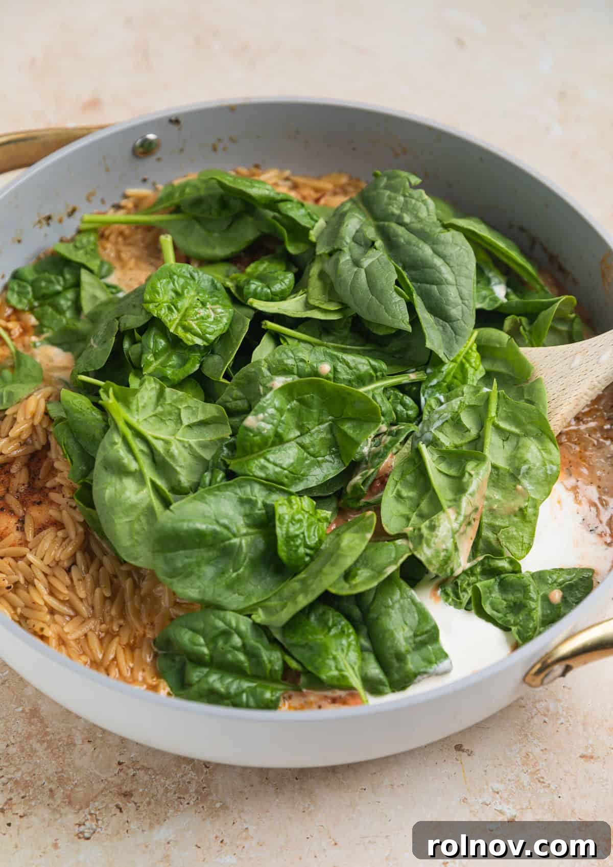 Rich Creamy Chicken Orzo 10 Baby spinach, cream and parmesan added to pot with wooden spoon.