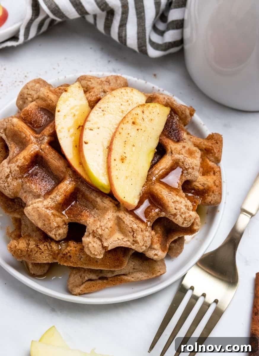 Crispy vegan waffles drizzled with maple syrup, garnished with fresh apple slices and a sprinkle of cinnamon.