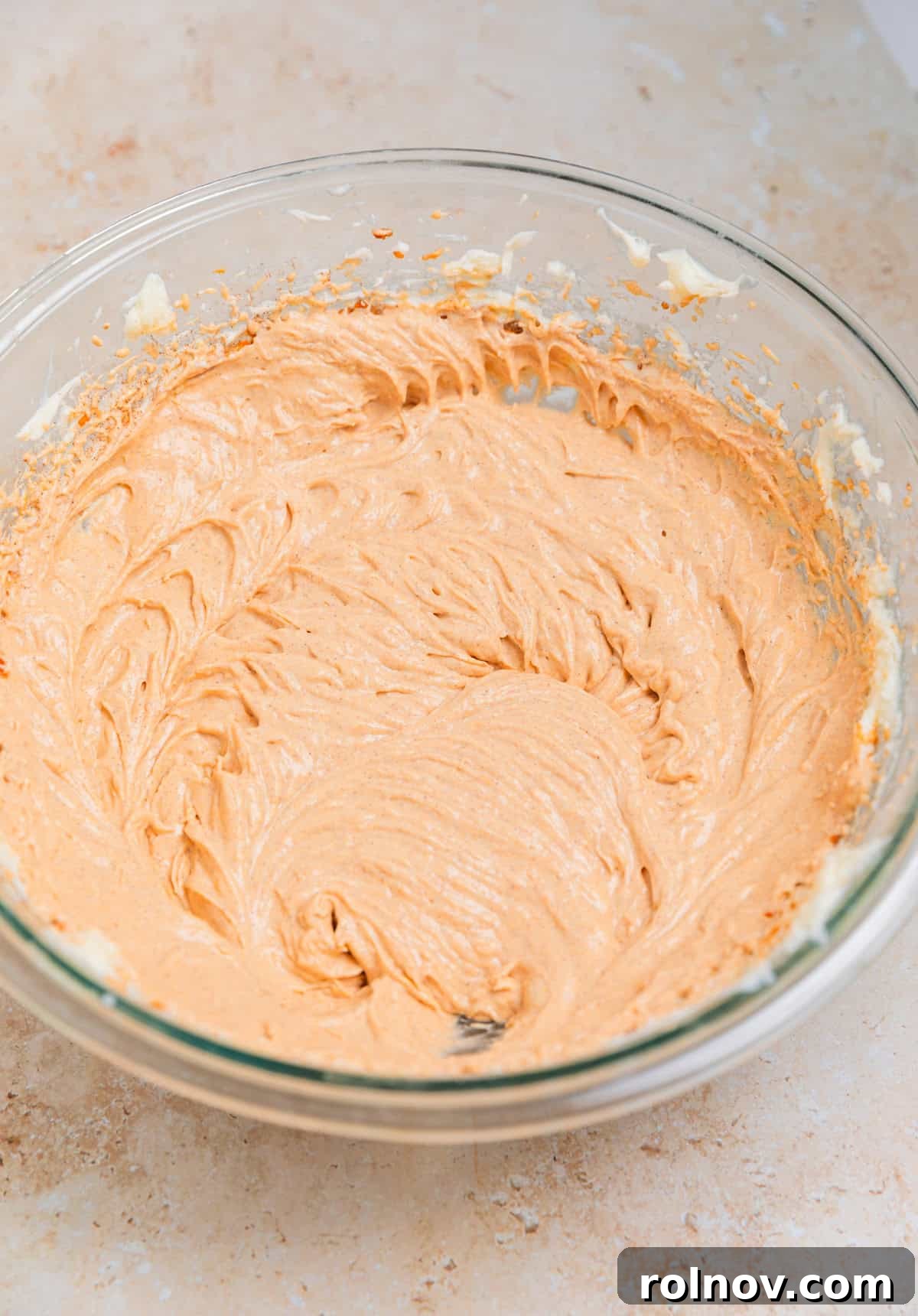 The vibrant orange pumpkin no bake cheesecake filling prepared and smoothed in a glass bowl, ready for whipped cream.