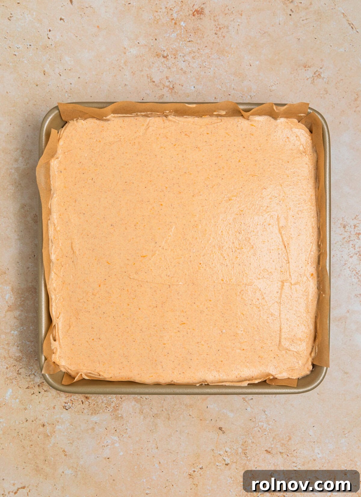 The prepared no bake pumpkin cheesecake in the square pan, with the filling smoothly spread over the crust, ready for chilling.