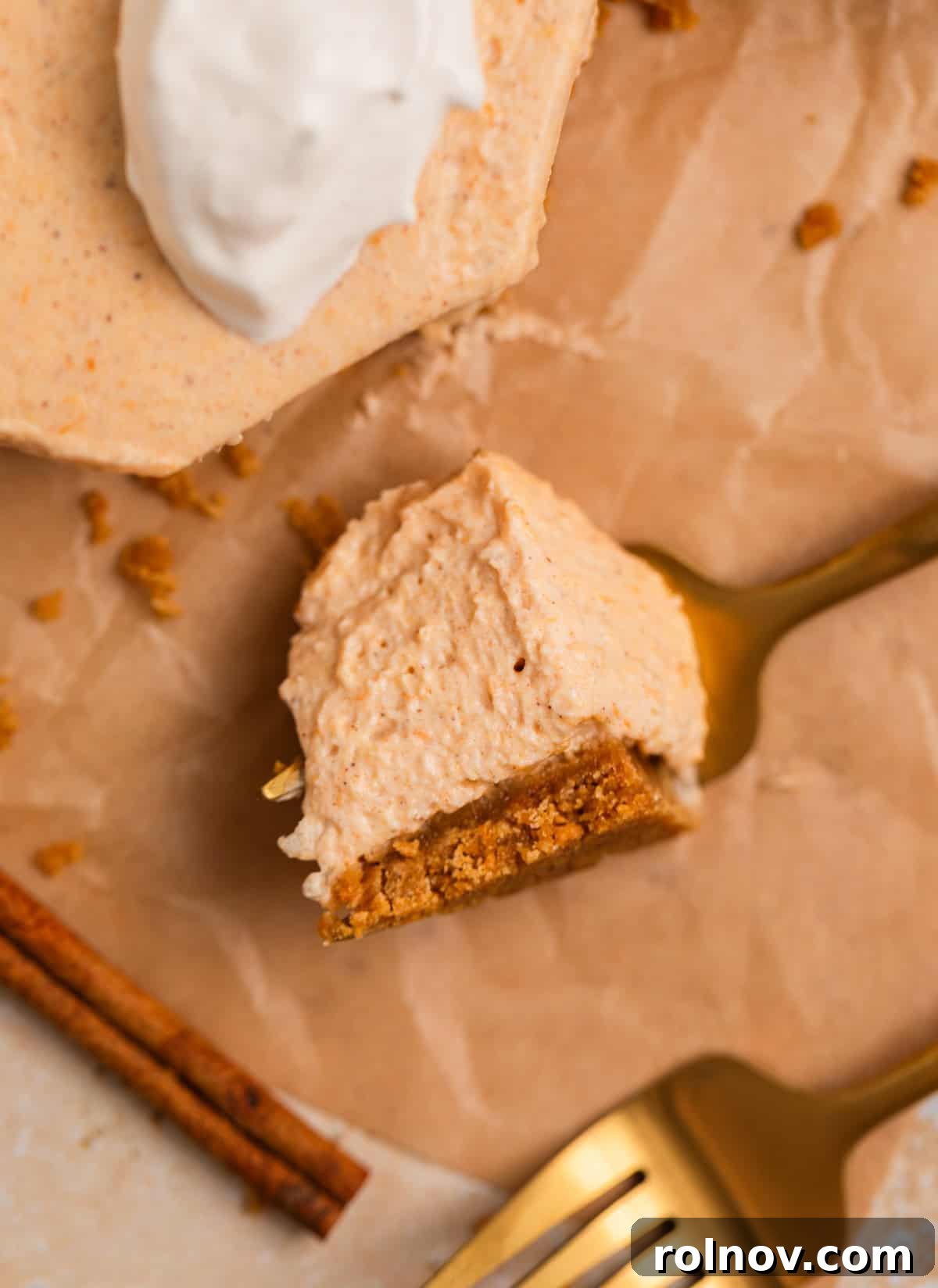A fork holding a piece of pumpkin cheesecake, with a cinnamon stick and another fork on the side, ready to be enjoyed.