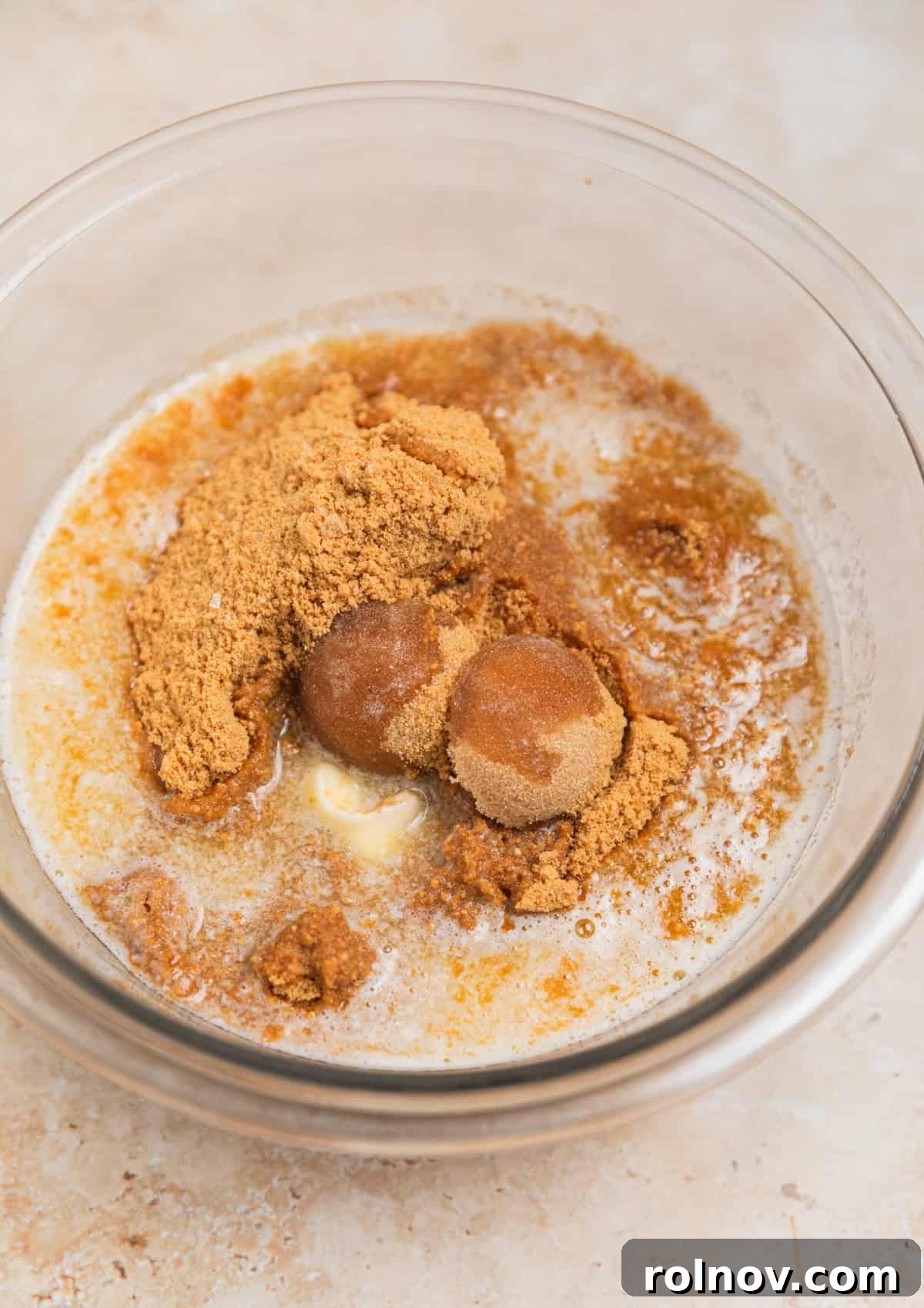 Brown sugar and melted butter being combined with ginger snap cookie crumbs in a clear glass bowl.