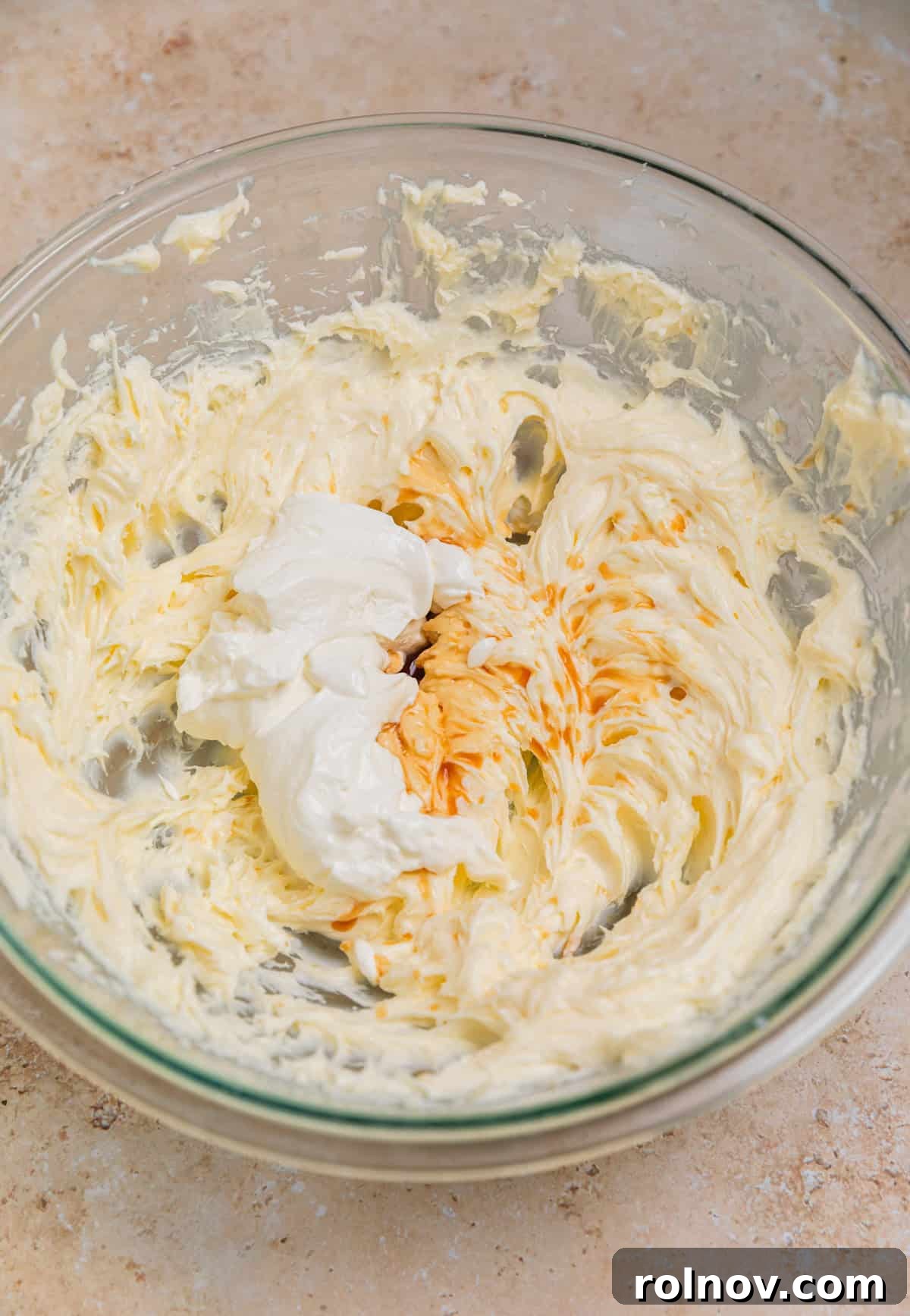 The cream cheese mixture with vanilla extract and room temperature sour cream added, being mixed until smooth.
