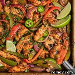 Baked chicken fajitas on sheet pan with spatula scooping onto the pan, featuring colorful bell peppers and onions.