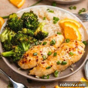 Baked orange chicken sheet pan dinner served on plate with white rice and orange slices, featuring vibrant, sticky chicken.