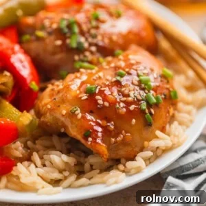 Honey garlic chicken thighs over rice with sliced bell peppers and chopsticks, featuring a glossy, sticky glaze.