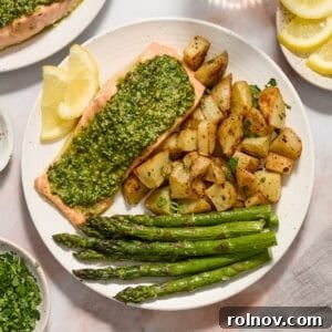 Pesto salmon dinner on white plate with roasted potatoes, asparagus and two lemon slices, highlighting vibrant green pesto.