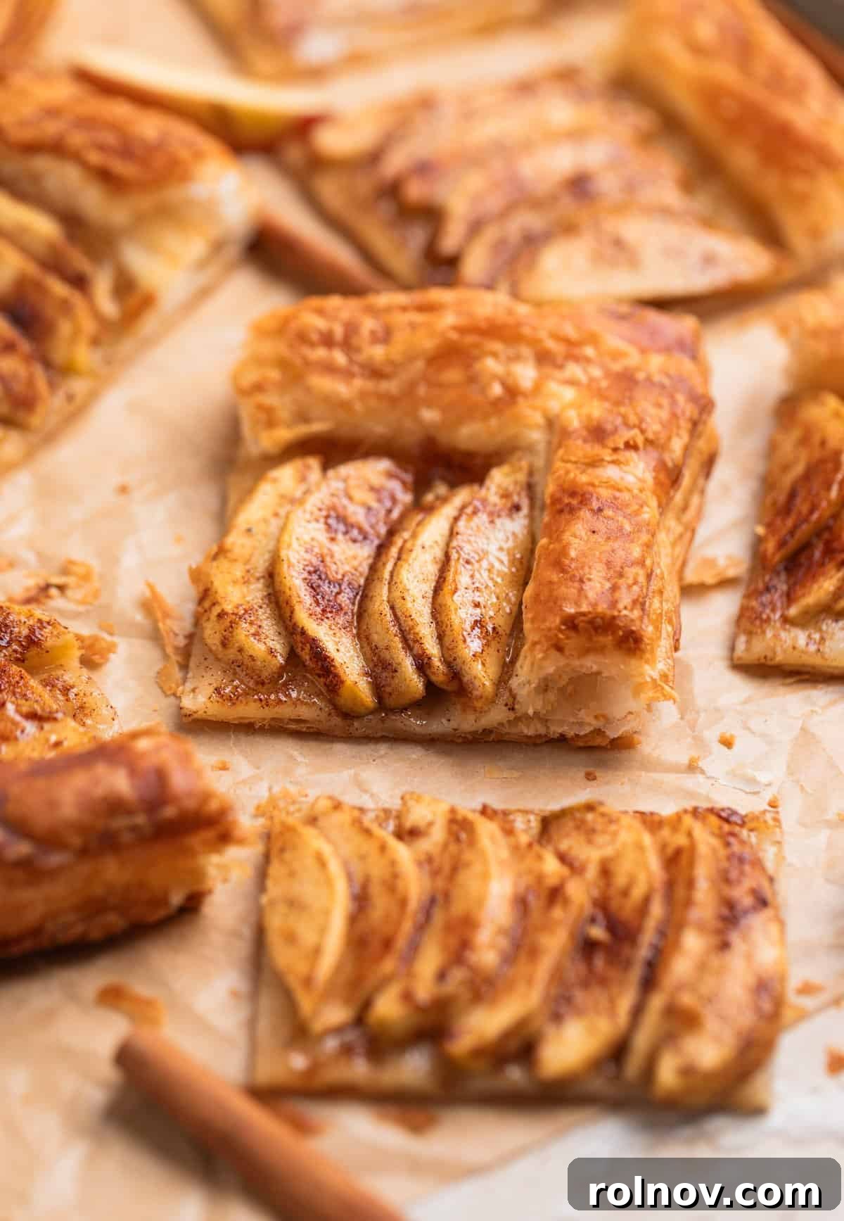 Flaky Apple Delight 2 Puff pastry and apple tarts sliced and arranged on parchment with cinnamon sticks surrounding.