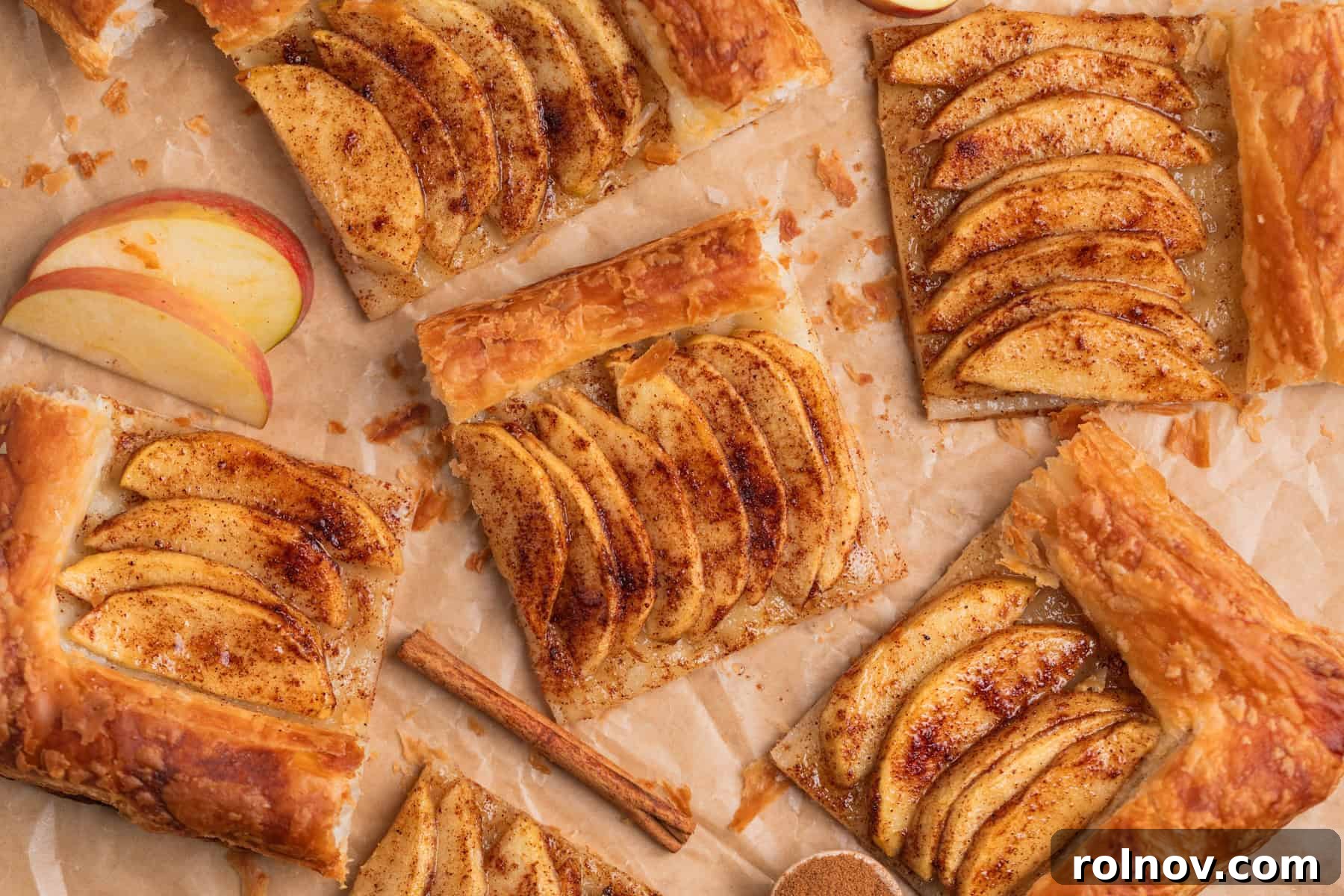 Flaky Apple Delight 3 Puff pastry apple tarts arranged on parchment with apple slices and cinnamon sticks.