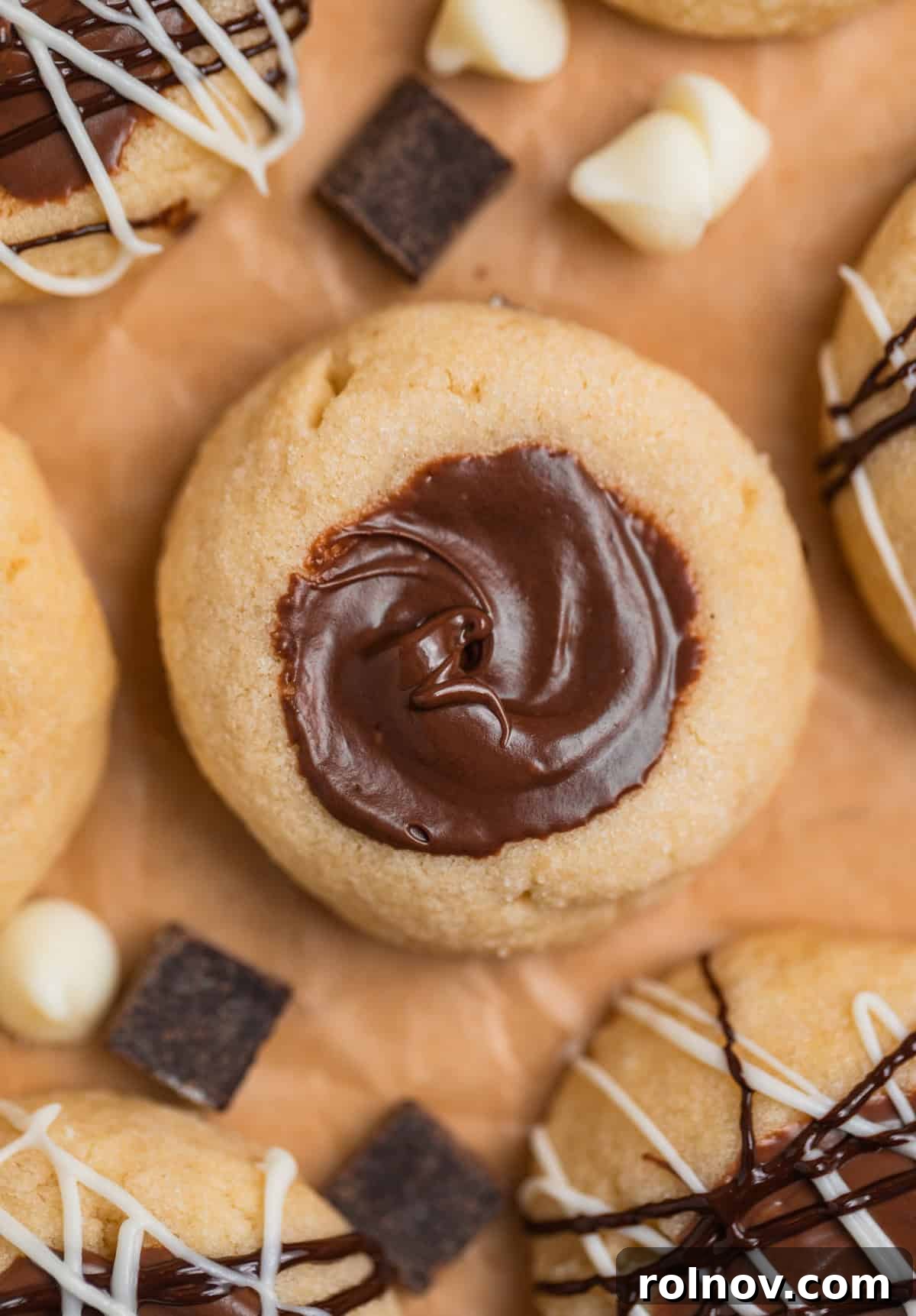 Irresistible Nutella Thumbprints 2 Nutella thumbprint cookies arranged on parchment with dark and white chocolate chips sprinkled around.