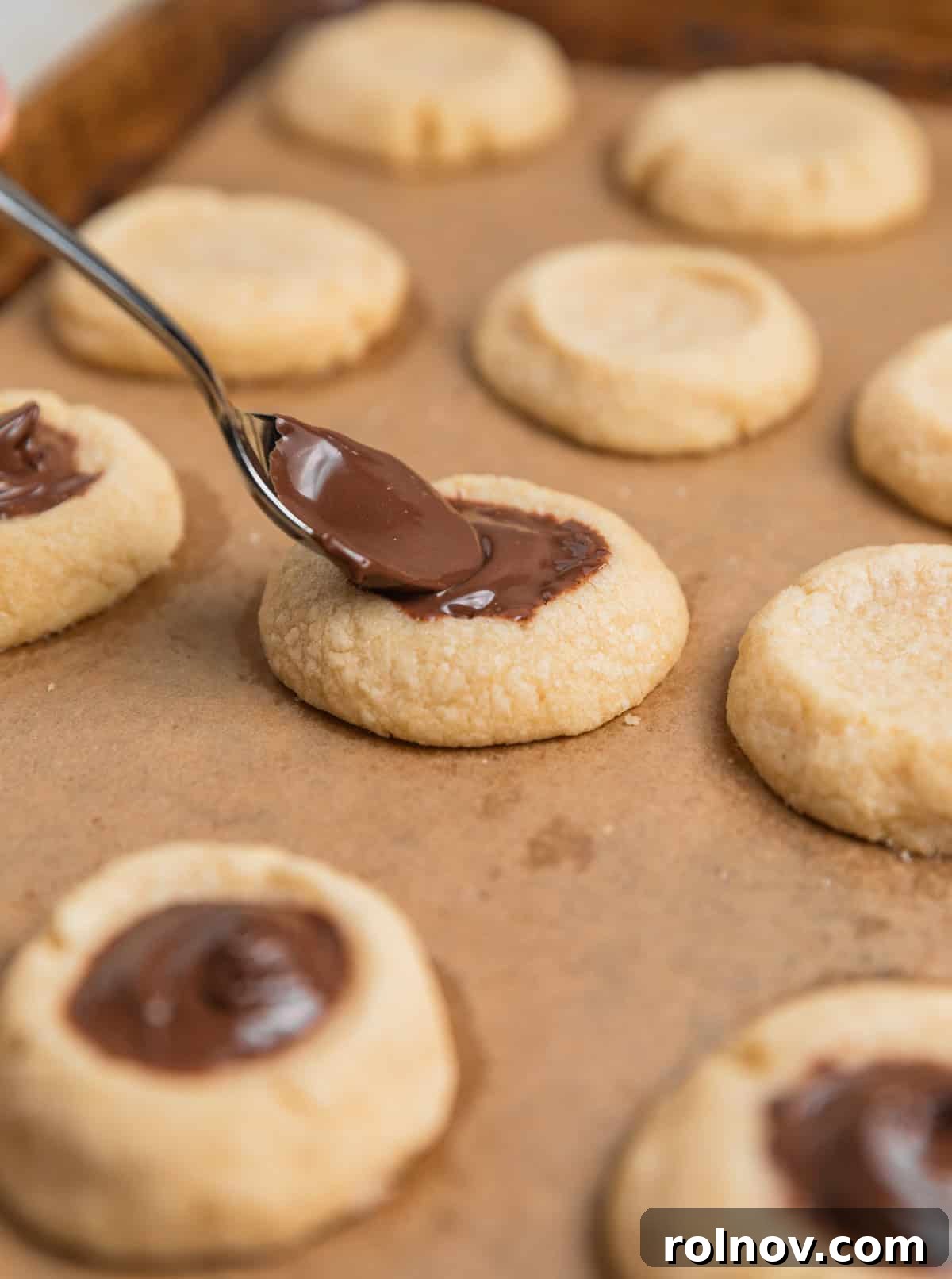 Irresistible Nutella Thumbprints 12 Nutella spooned into thumbprint impressions of cookies on sheet pan.