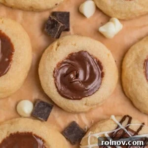Irresistible Nutella Thumbprints 14 Nutella cookies arranged on parchment with white and dark chocolate chips arranged around the cookies.