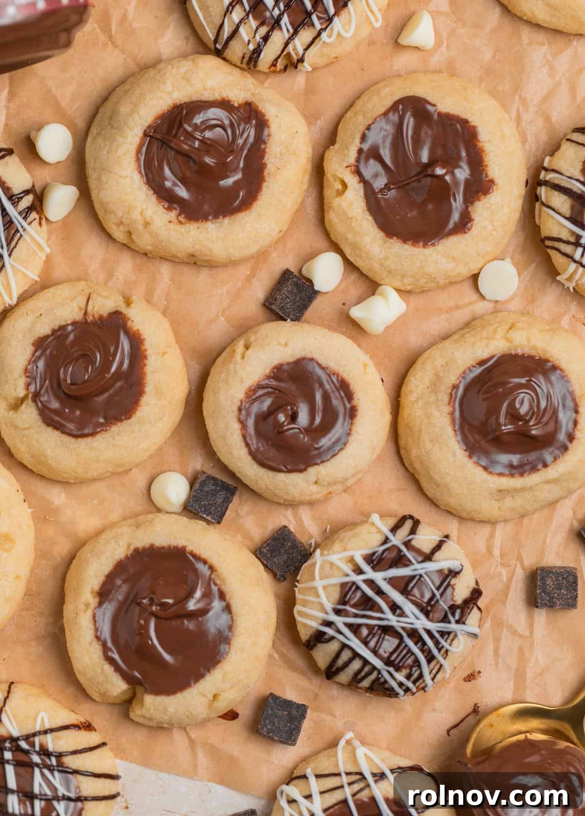 Irresistible Nutella Thumbprints 3 Nutella thumbprint cookies on brown parchment with white and dark chocolate drizzle on some of the cookies.