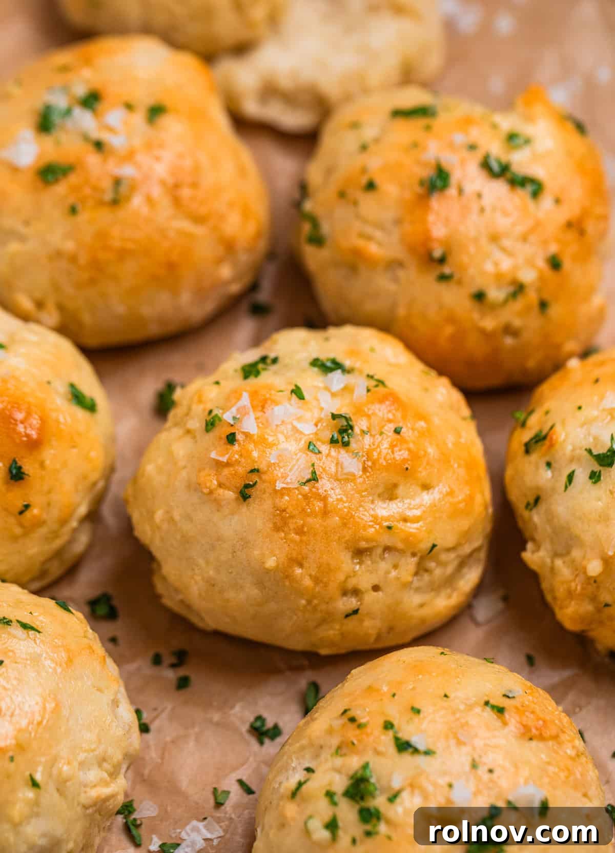 No yeast dinner rolls topped with garlic butter, flaked sea salt and parsley on parchment.