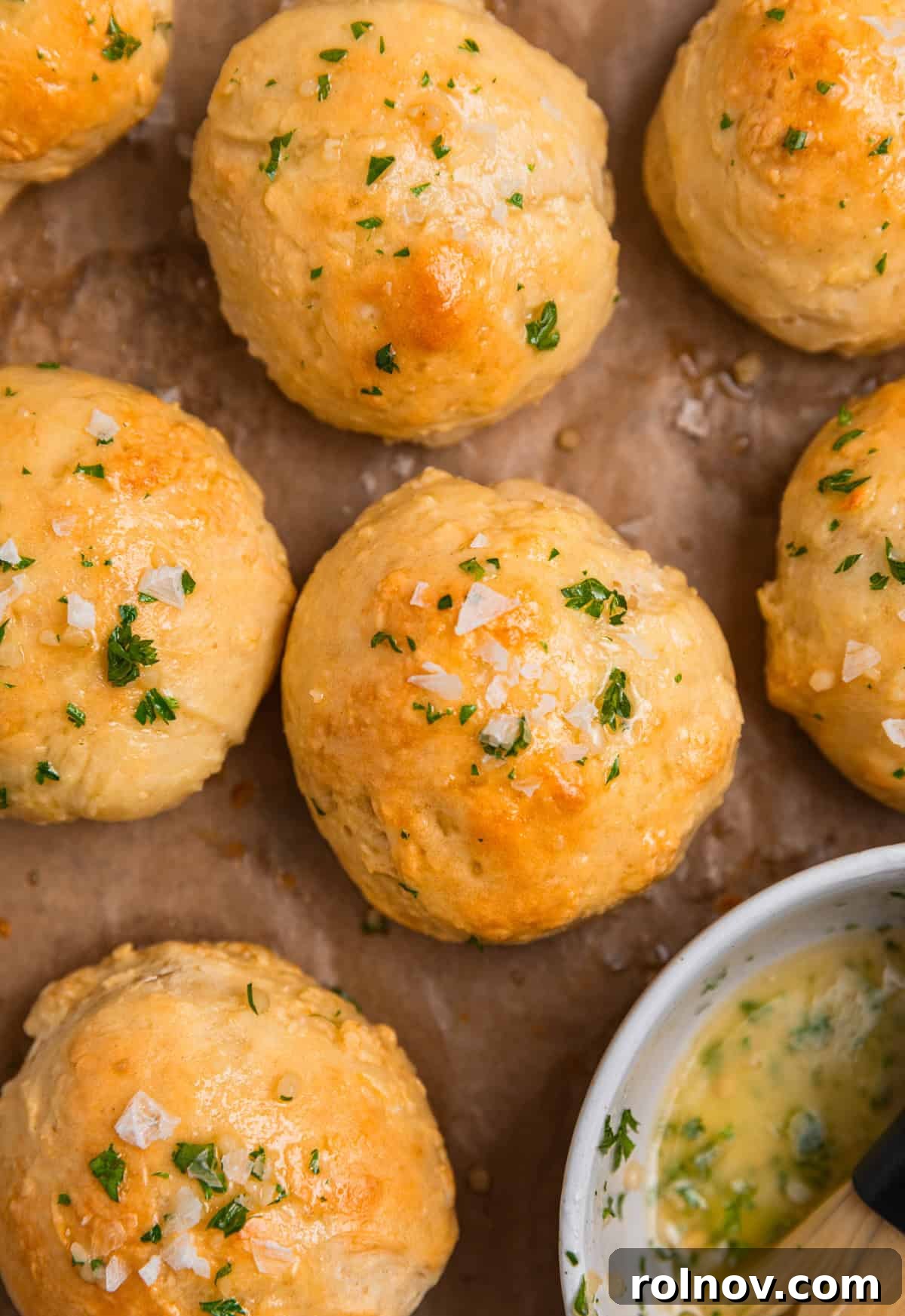 Garlic herb butter in bowl next do dinner rolls.