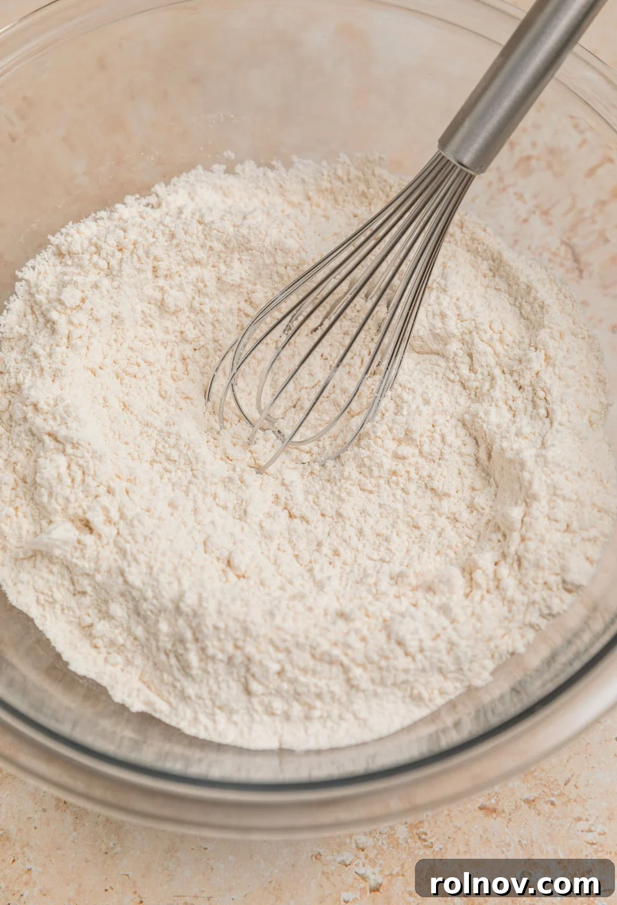 Flour mixture in glass bowl with whisk propped in bowl.