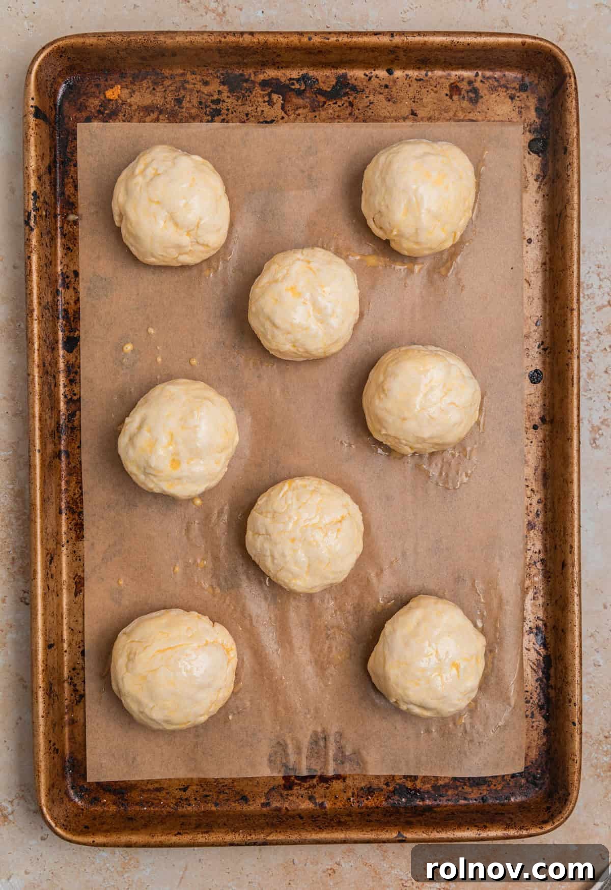 Sheet pan with dinner rolls that have been brushed with egg wash.