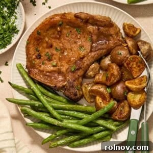 Sheet pan pork chops served on plate with potatoes and green beans, ready to eat and garnished with fresh herbs.