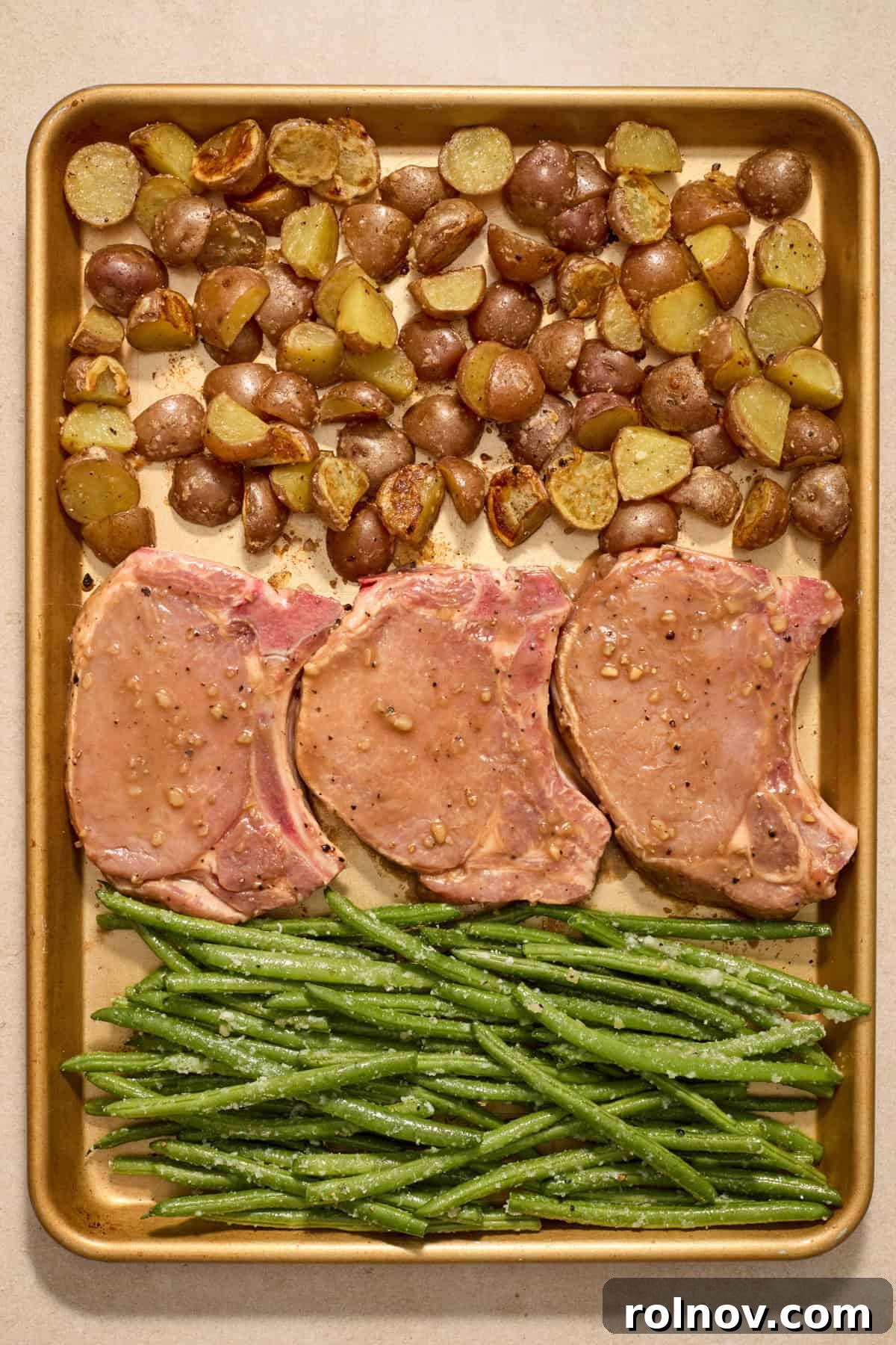 Quick & Flavorful Sheet Pan Pork Chops 9 A baking sheet artfully arranged with partially cooked potatoes, marinated pork chops, and seasoned green beans, ready to be placed back in the oven for final roasting.