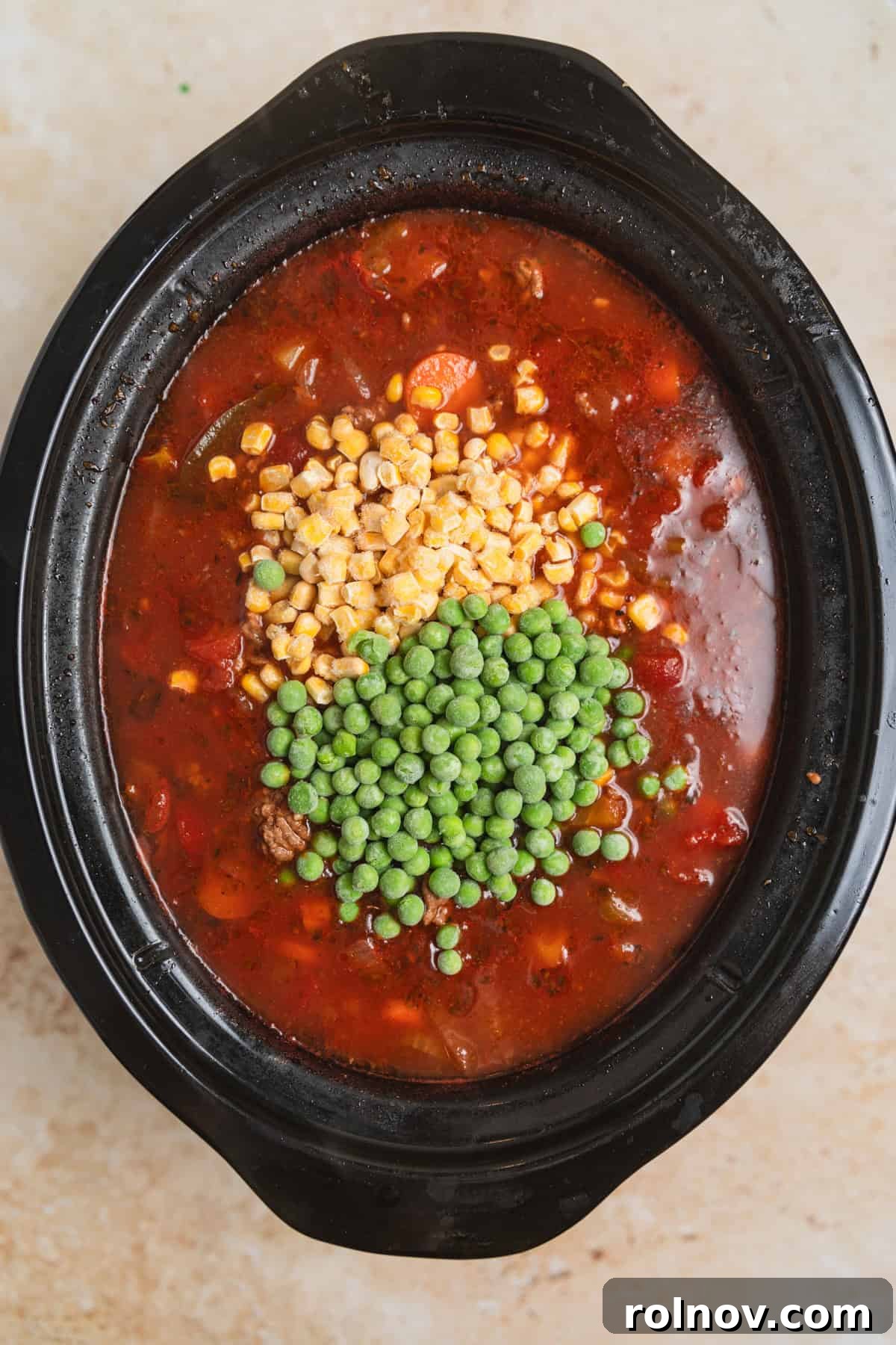 Hearty Slow Cooker Ground Beef Soup 8 Frozen peas and corn being stirred into slow cooker with hamburger soup.