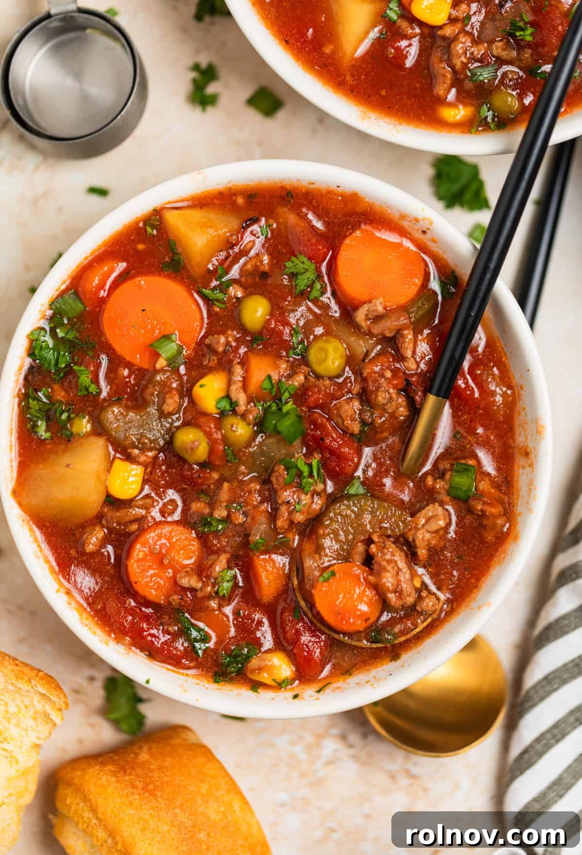 Hearty Slow Cooker Ground Beef Soup 10 Bowl of hamburger soup with vegetables, topped with shredded cheese and a spoon scooping into it.