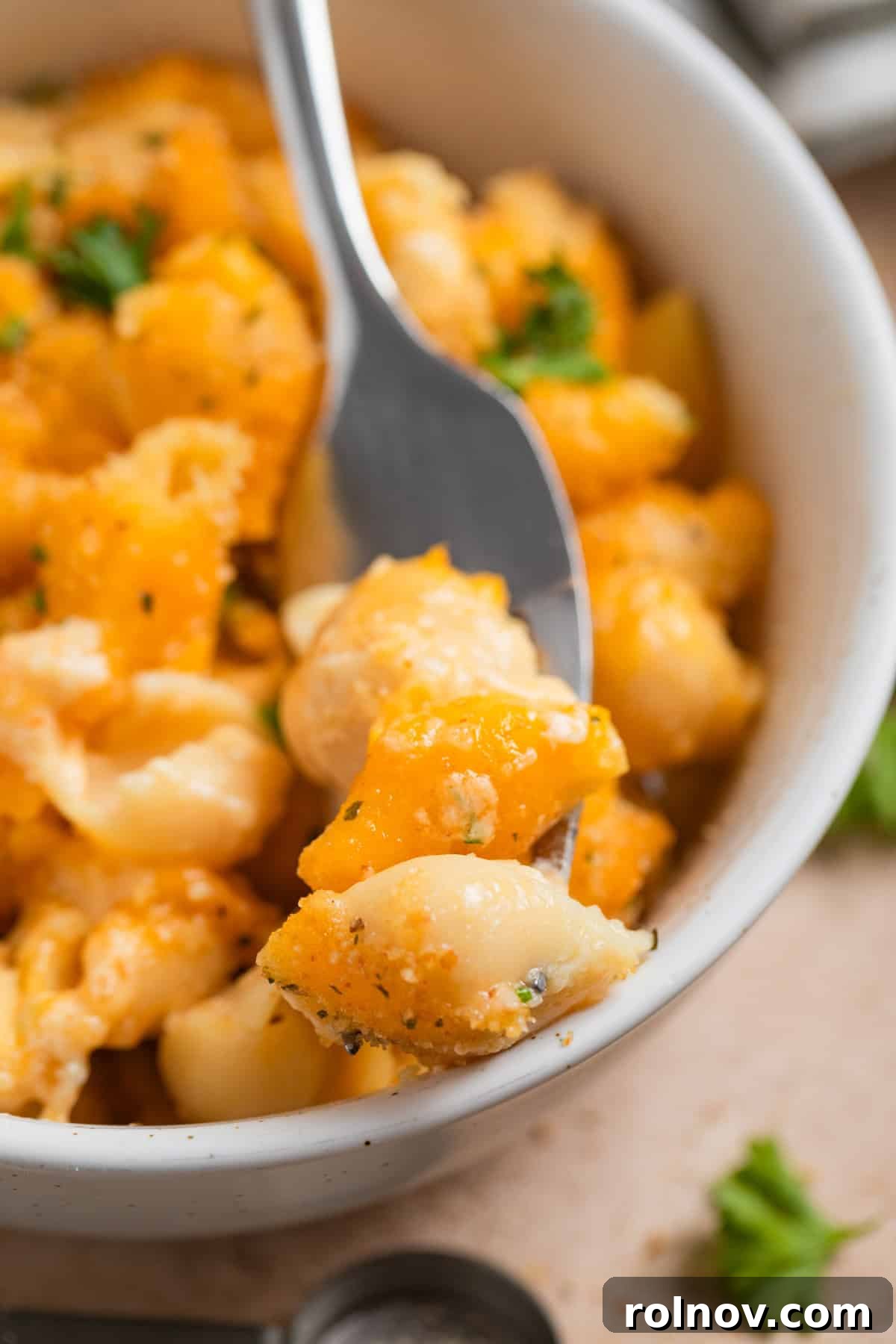 Muscle Mac 3 A fork lifts a generous portion of creamy protein macaroni and cheese from a bowl, showcasing its rich texture.
