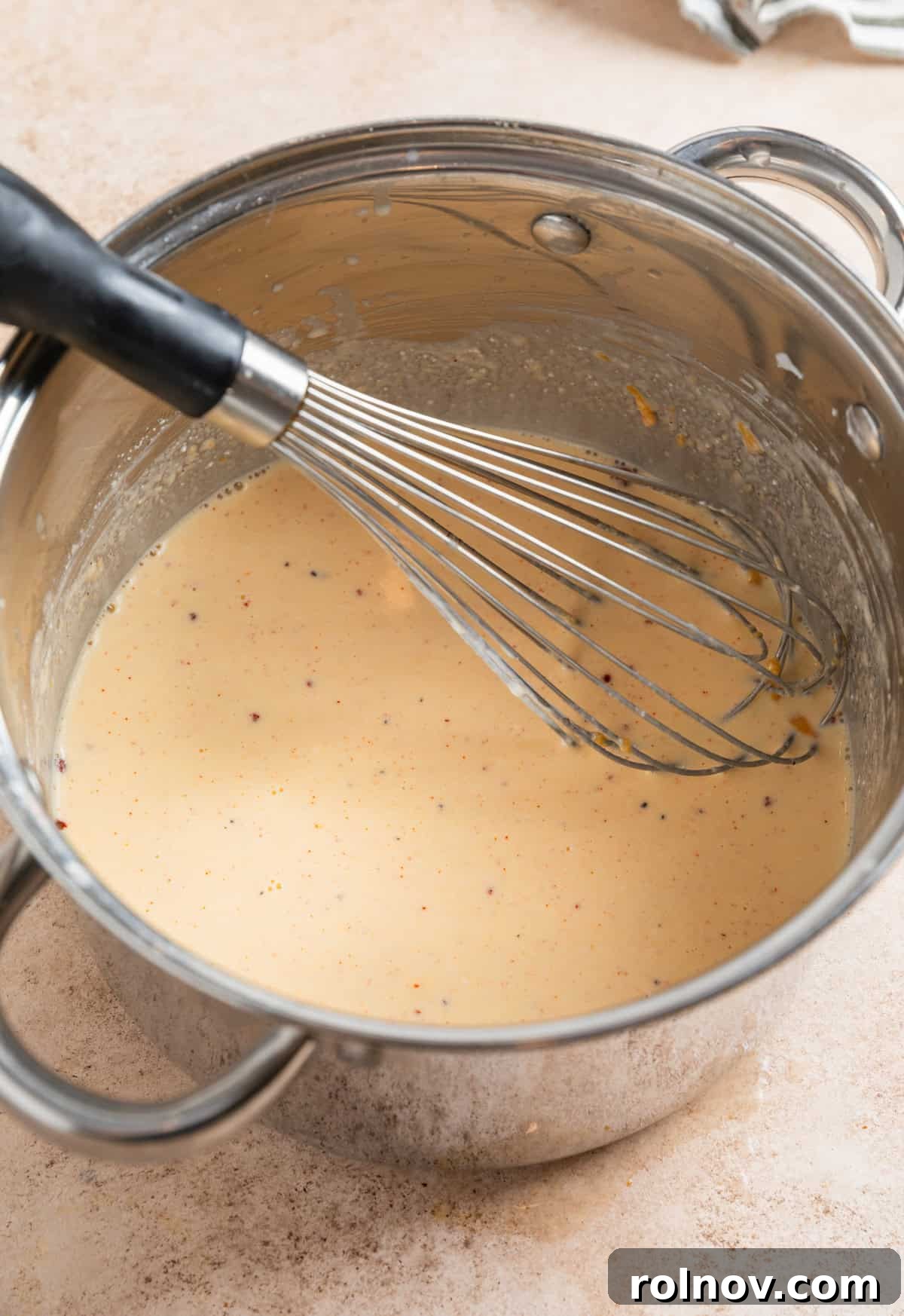 Muscle Mac 6 A whisk swirls a rich, smooth mac and cheese sauce in a large pot, showing perfect consistency.