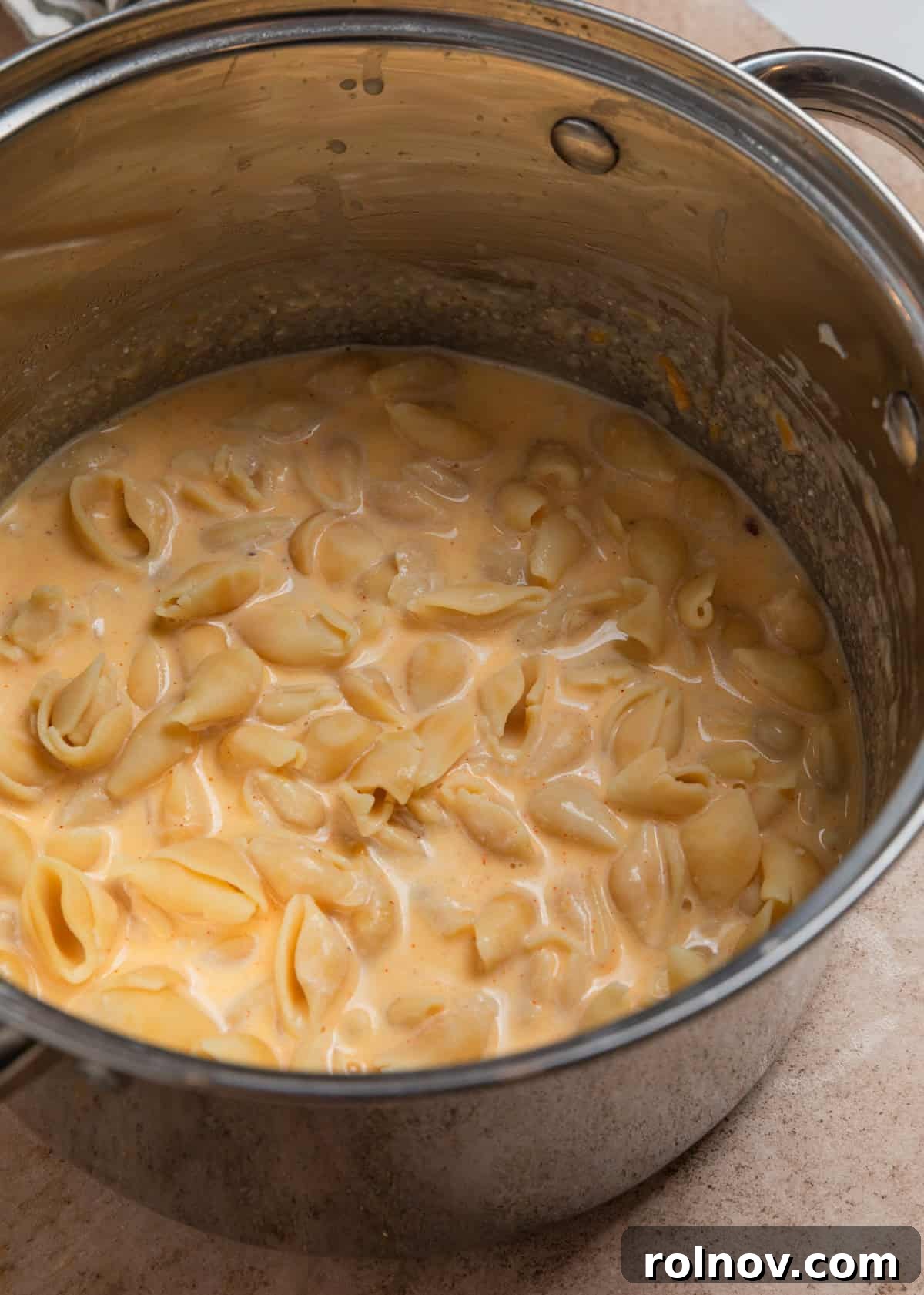 Muscle Mac 7 Cooked pasta being added and stirred into a large pot filled with creamy cheese sauce.