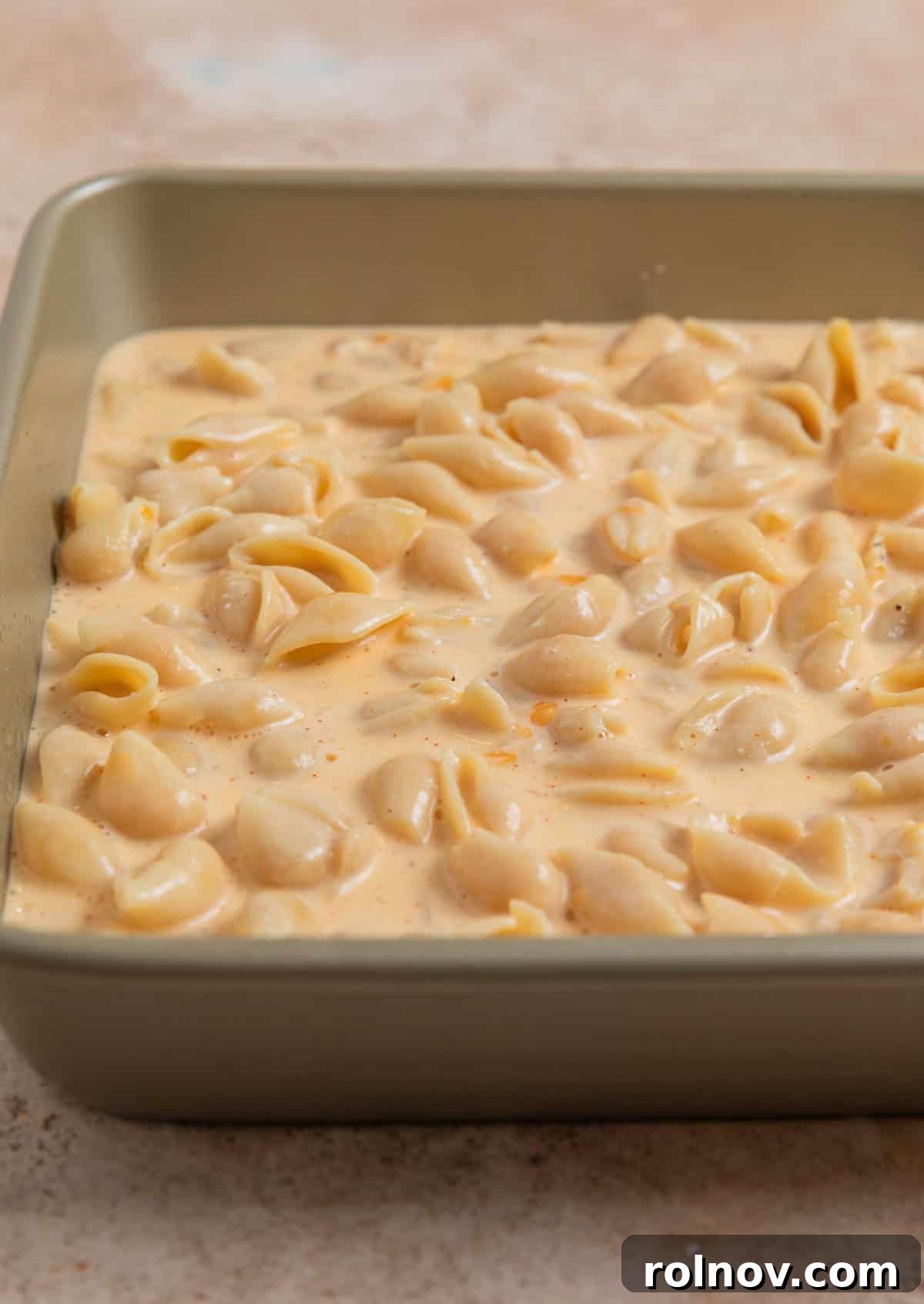 Muscle Mac 8 Protein macaroni and cheese mixture evenly spread in a square baking pan, ready for the oven.