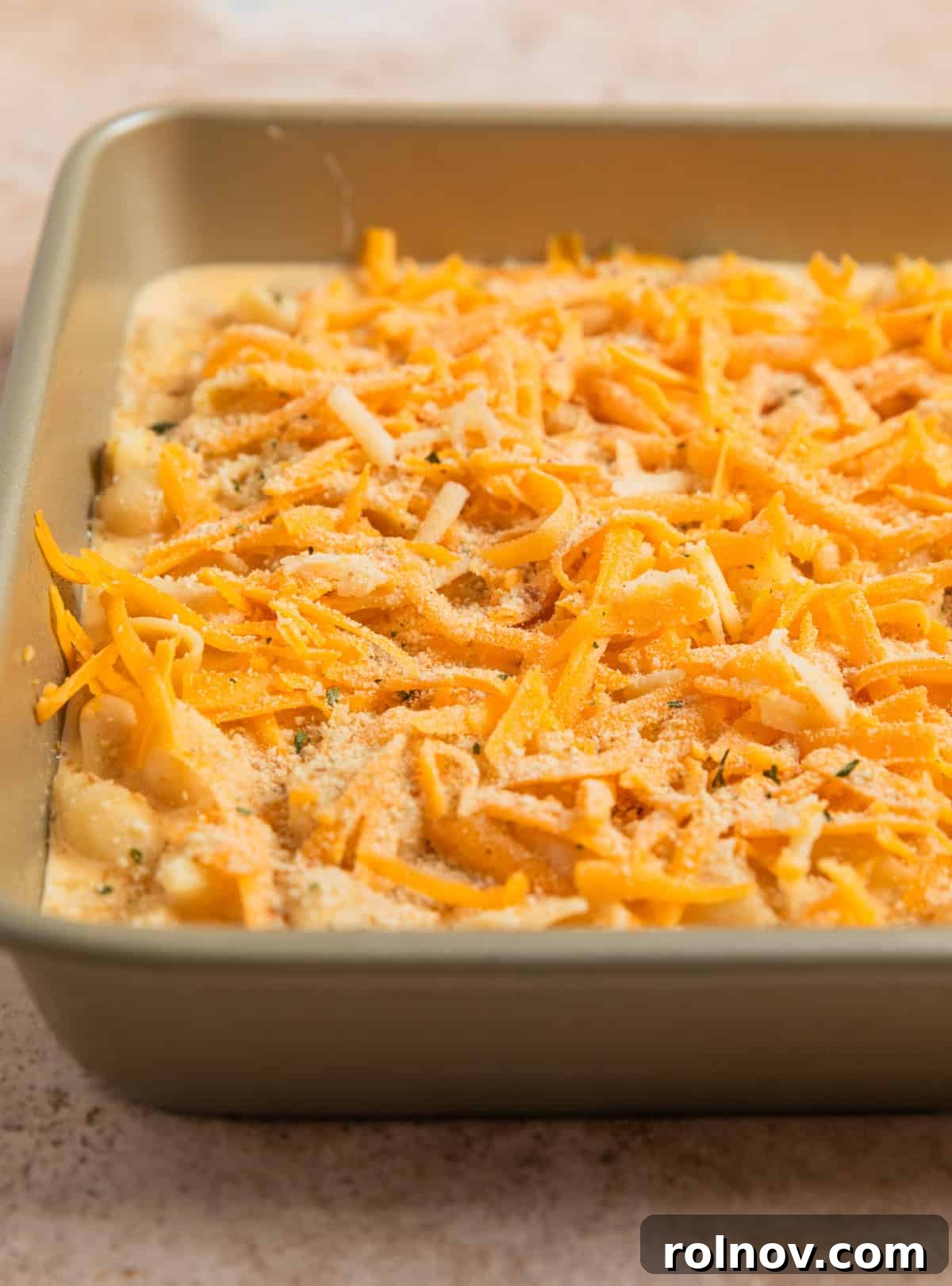 Muscle Mac 9 A close-up shot of shredded cheddar and white cheddar cheese topping the mac and cheese mixture in a baking pan, prior to baking.