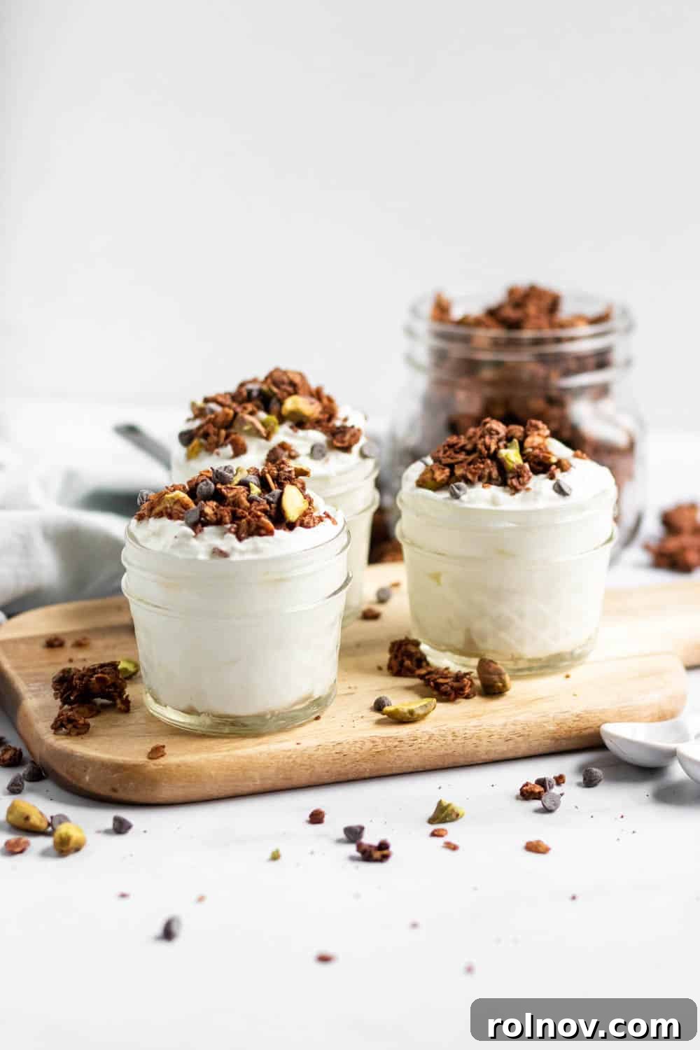 Sweet Salty Chocolate Pistachio Granola 3 Close-up of chunky chocolate granola with chocolate chips and pistachios on yogurt in clear jars, ready to be served.